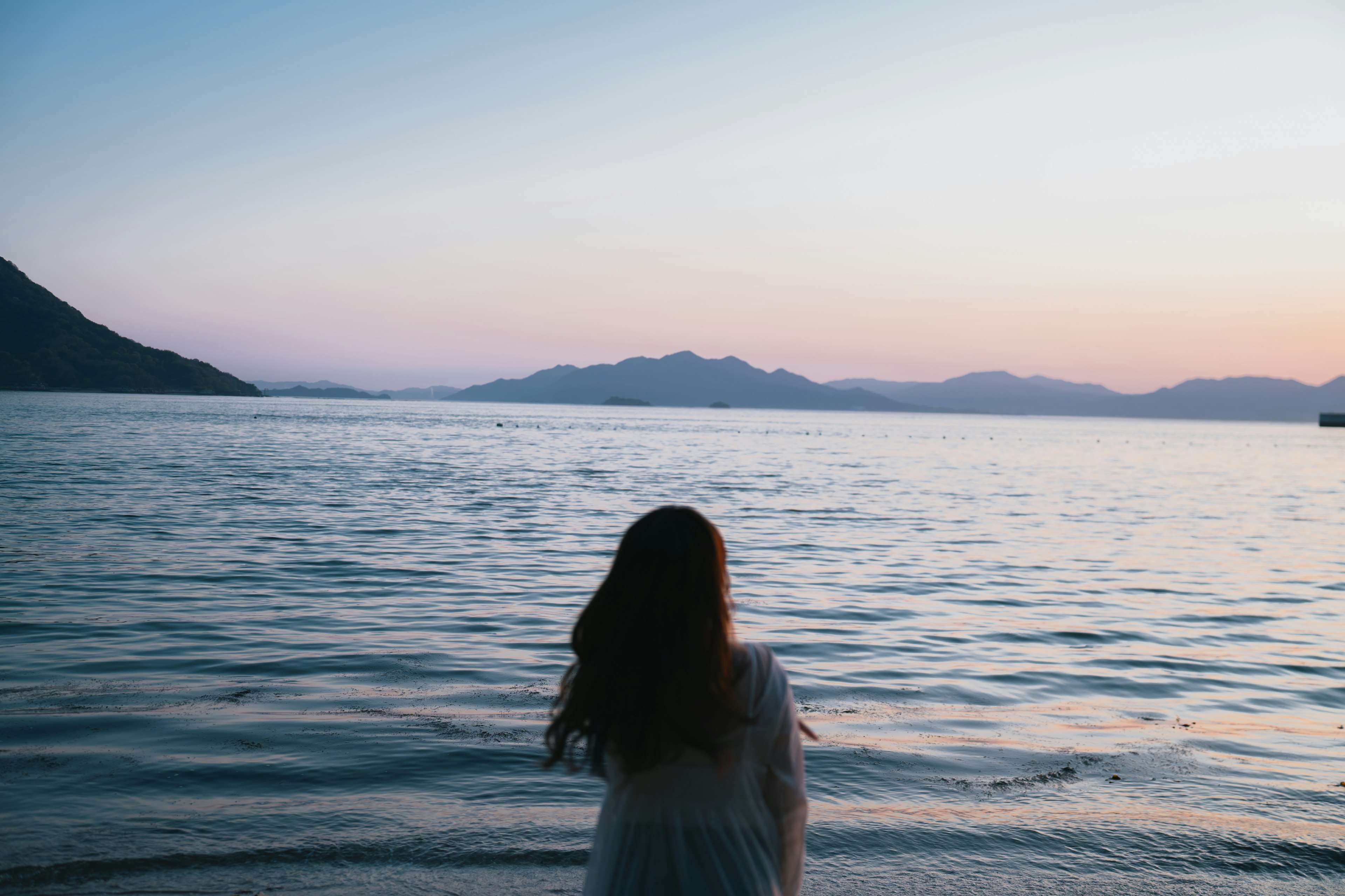 女性が海を見つめる夕暮れの風景