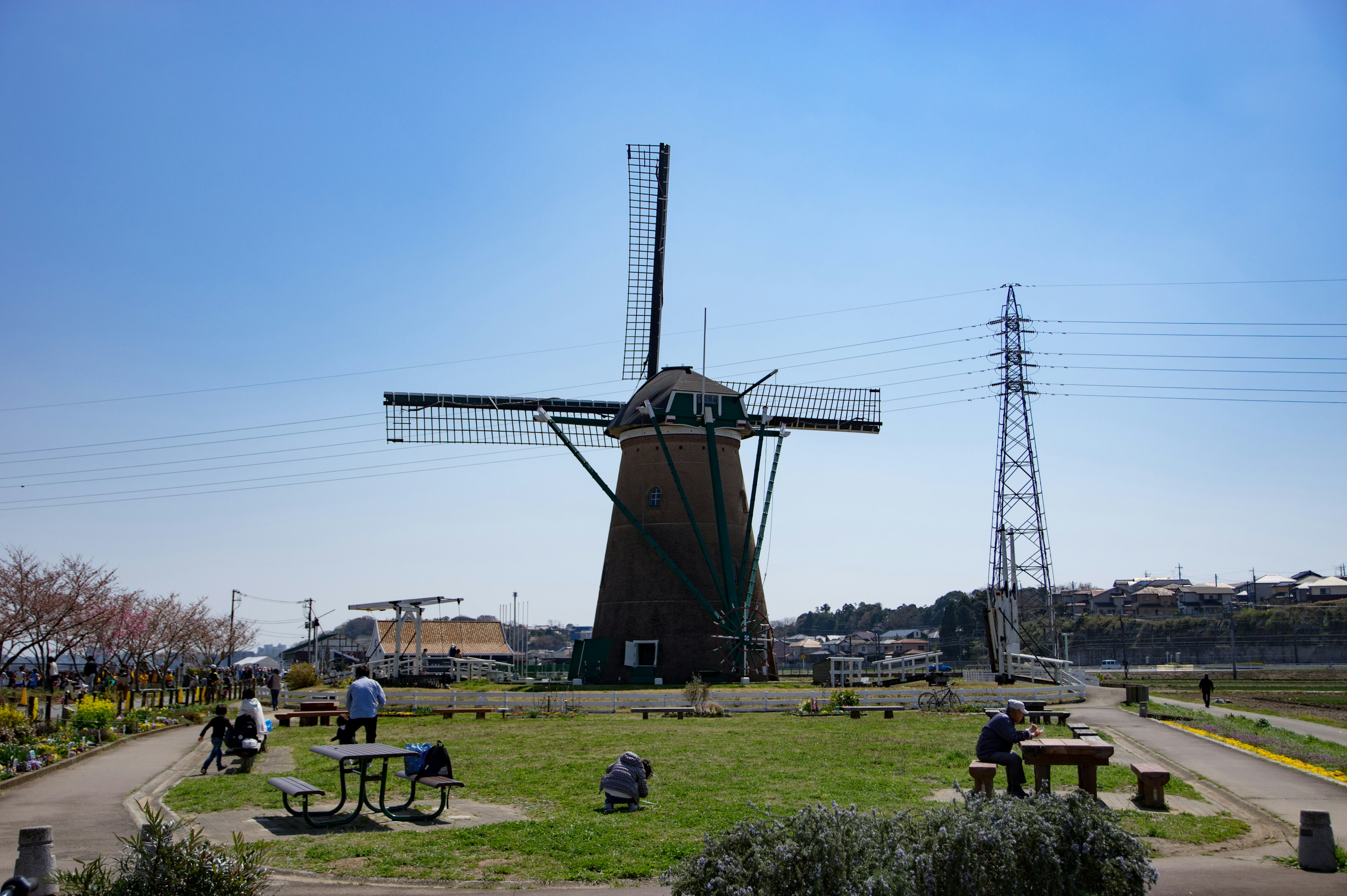 Paisaje con un molino de viento bajo un cielo azul y personas relajándose en un parque