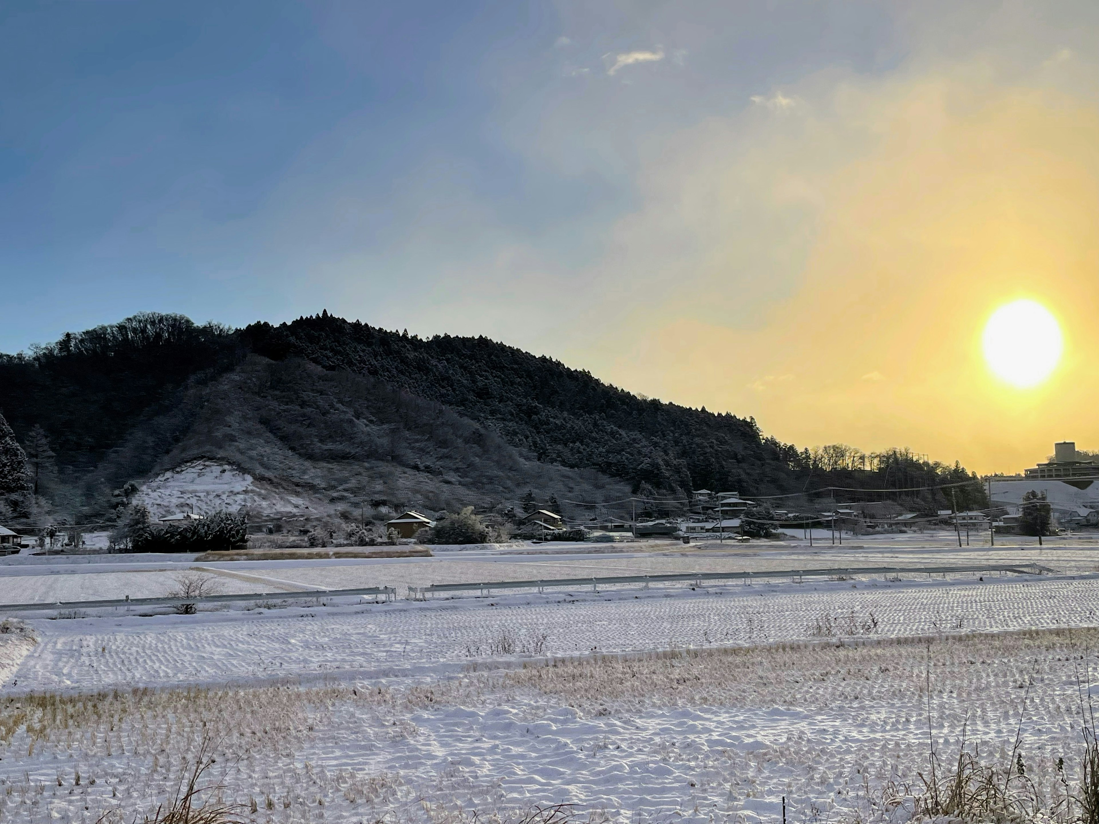 Snow-covered landscape with silhouetted hills and a setting sun