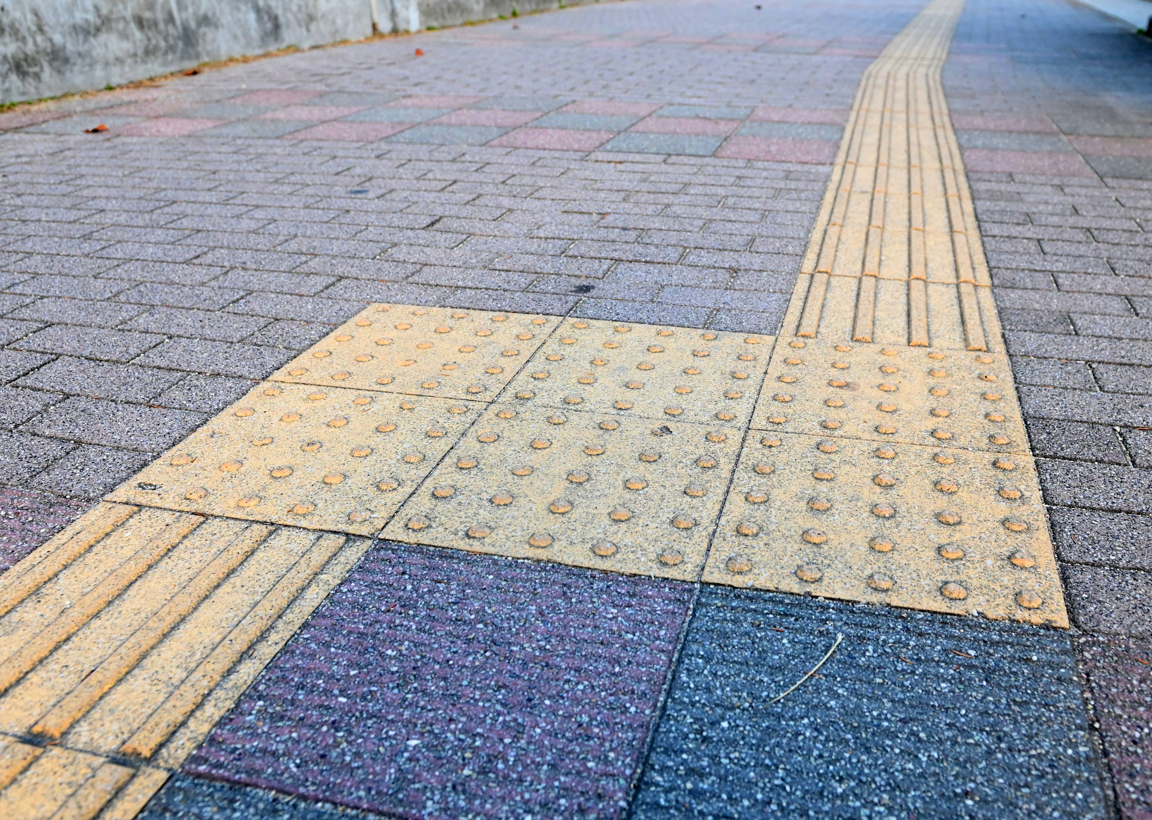 Sidewalk with yellow tactile paving and patterned stone tiles