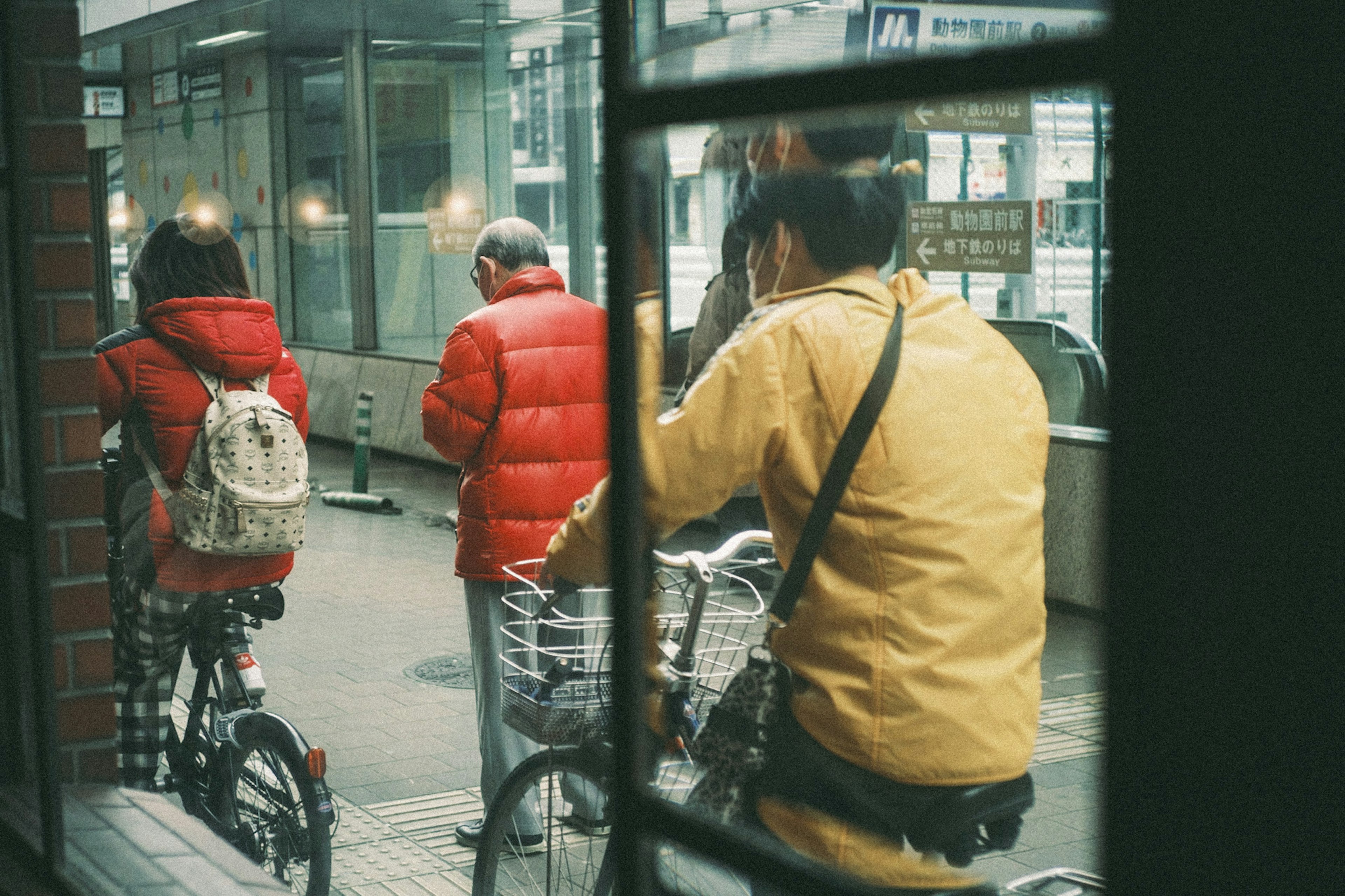 自転車に乗る人々と赤いダウンジャケットを着た二人が映る街の風景