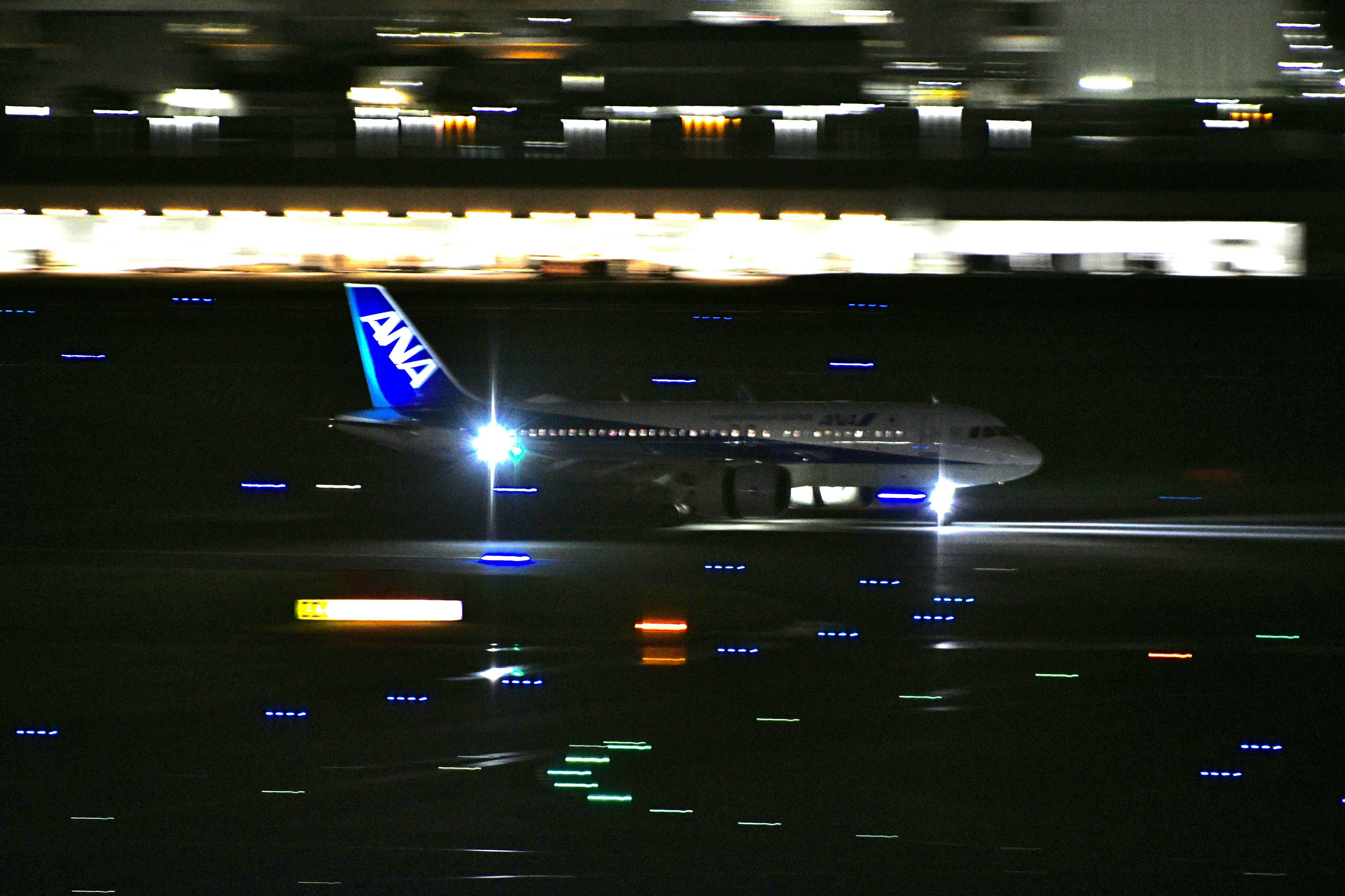 夜の空港で滑走するANAの飛行機明るいランプと流れる光の軌跡