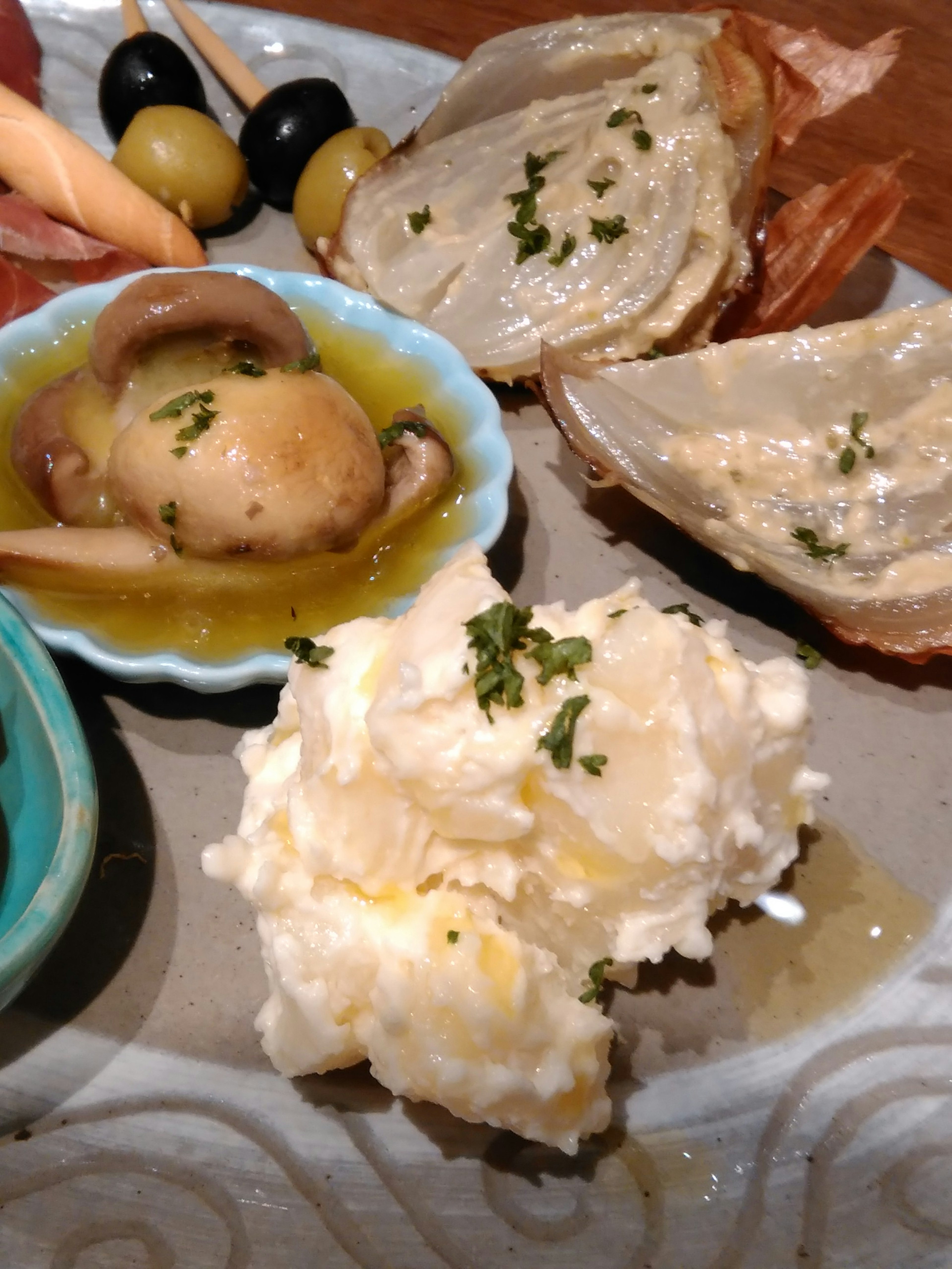 Un plato de aperitivos variados con aceitunas, alcachofas, champiñones, un dip cremoso cubierto de hierbas