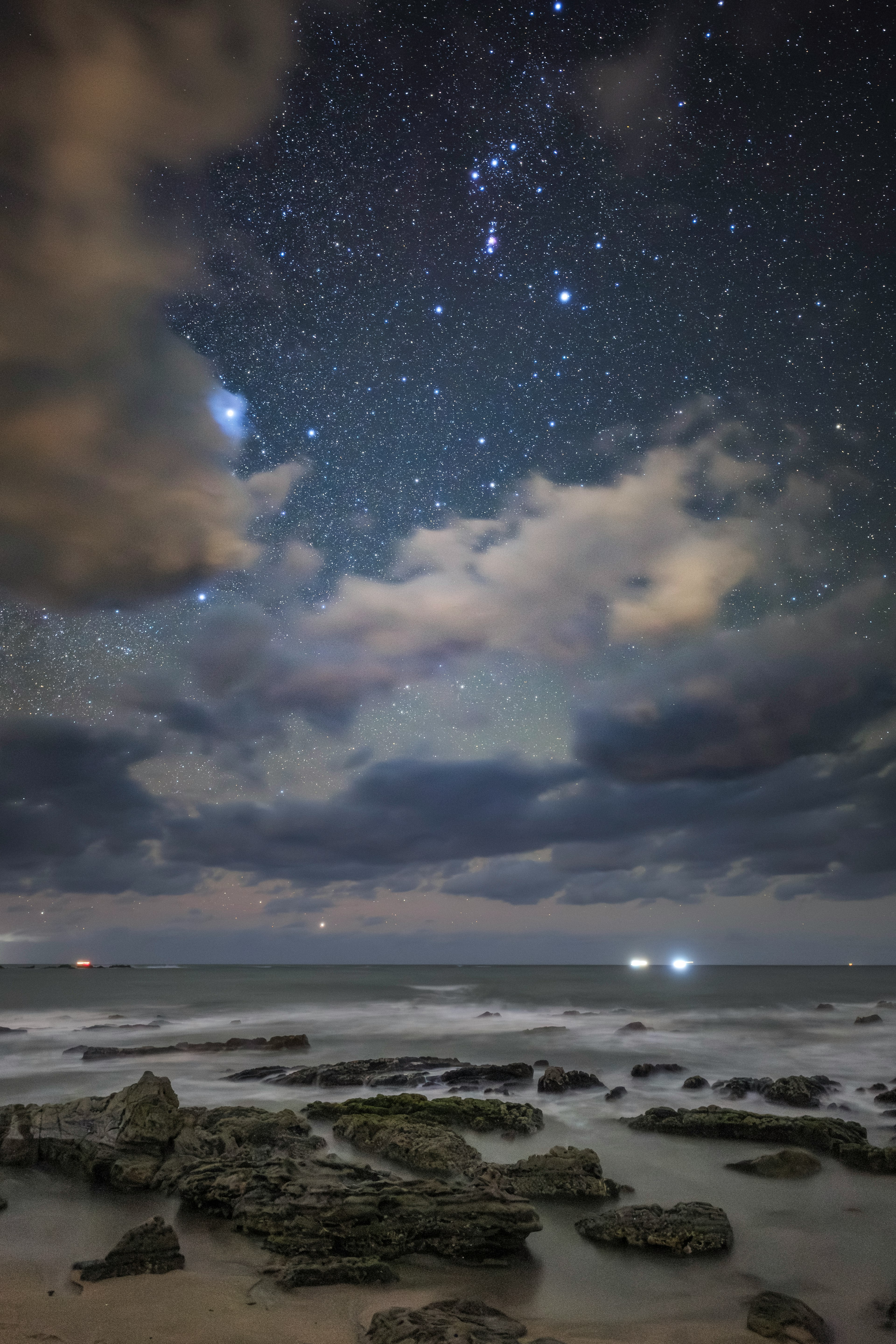 Cielo notturno sopra l'oceano con stelle luminose e nuvole