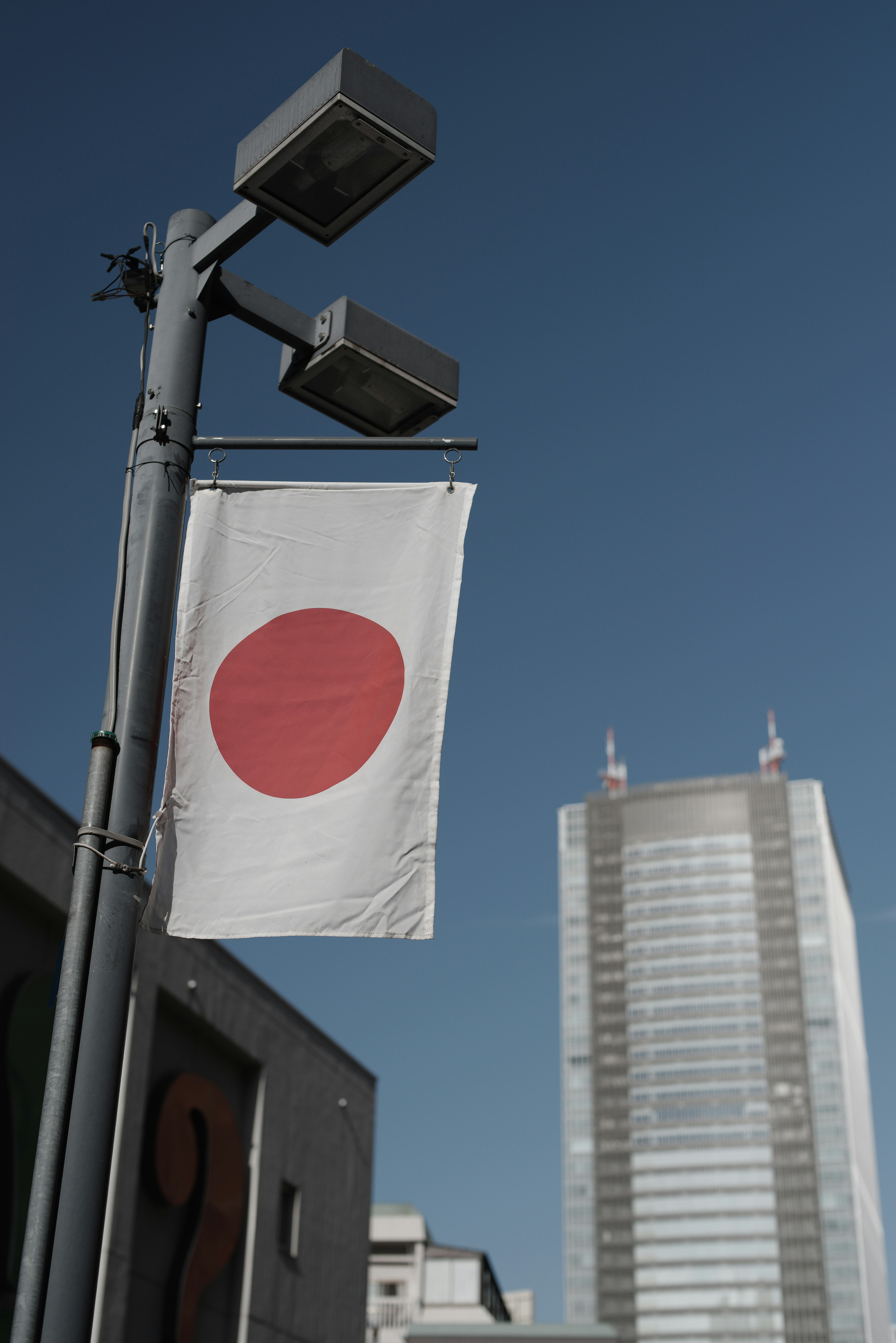 Lampadaire affichant le drapeau japonais avec un cercle rouge et un grand bâtiment en arrière-plan