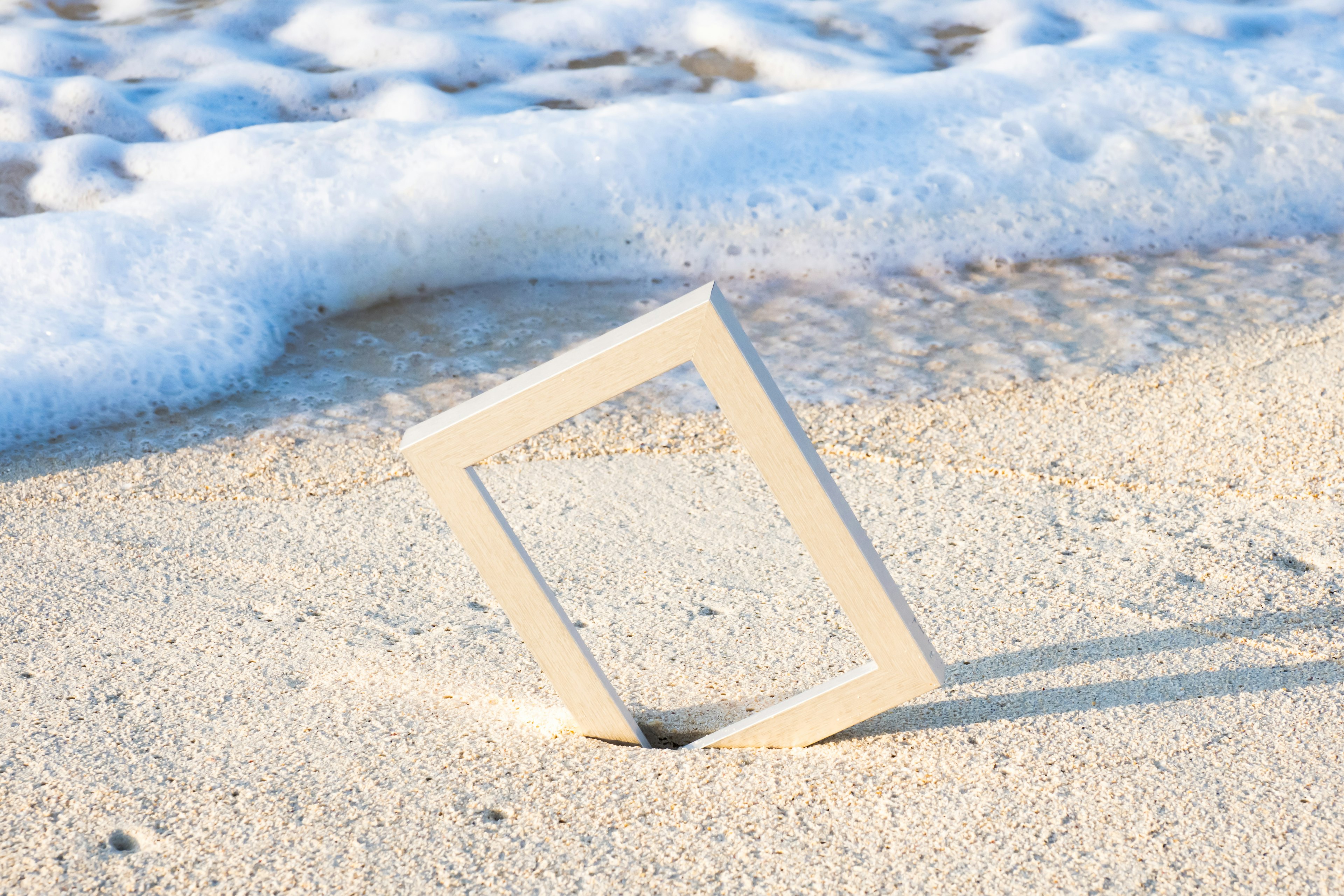 White frame placed on sandy beach with ocean waves