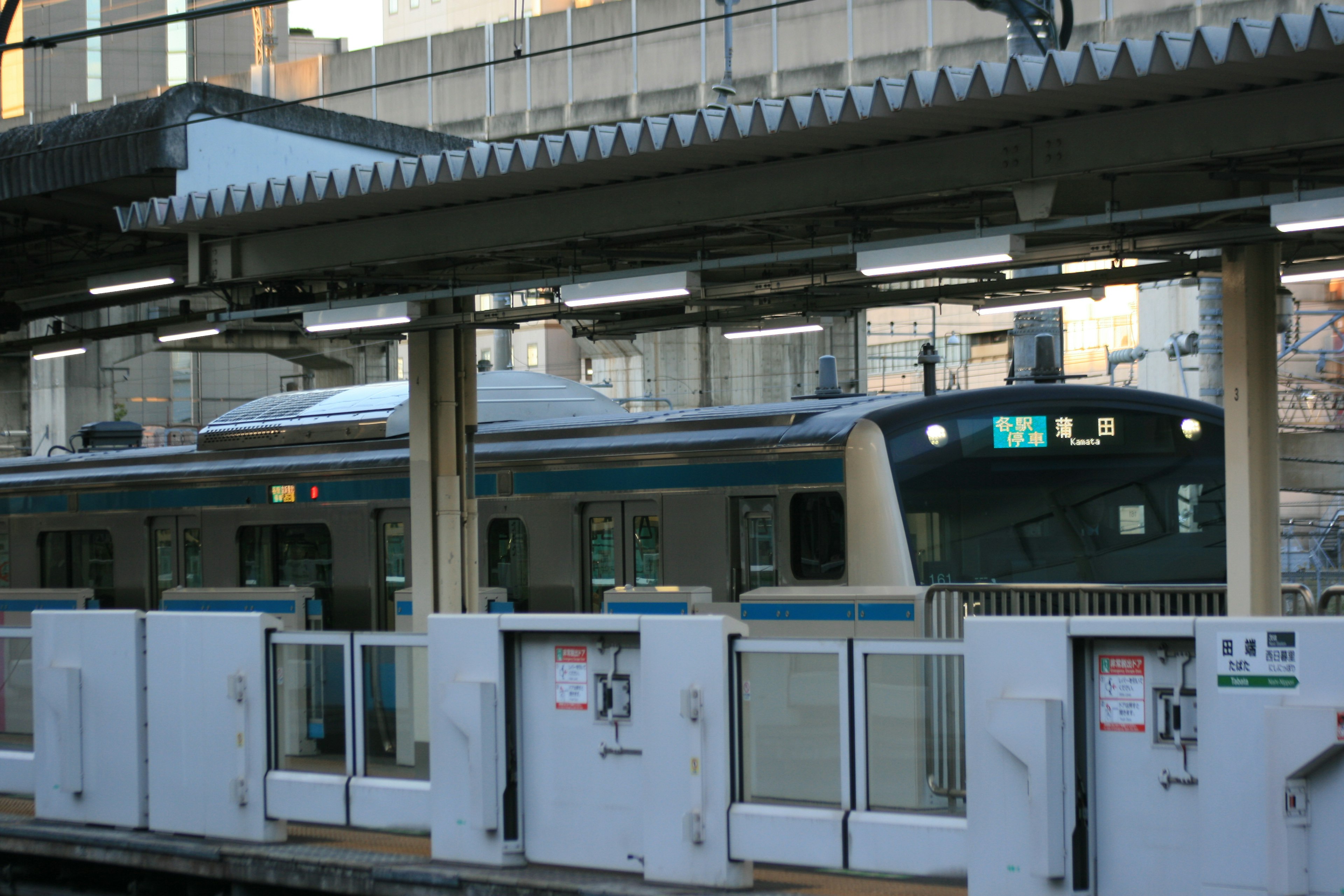 Sebuah kereta berhenti di stasiun dengan desain kereta modern dan arsitektur stasiun yang terlihat