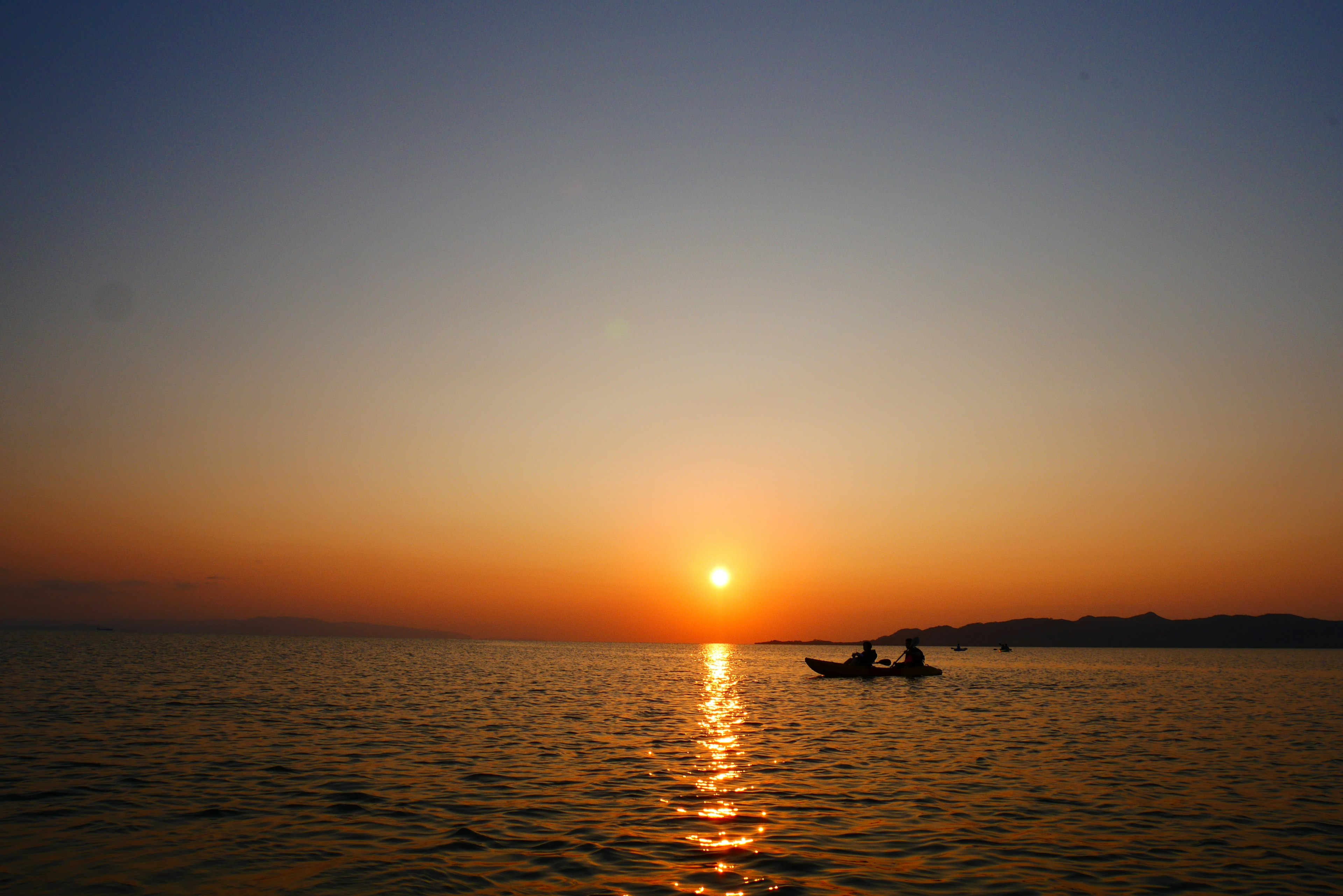 ชาวประมงสองคนในเรือกับพระอาทิตย์ตกที่สวยงามเหนือผืนน้ำ