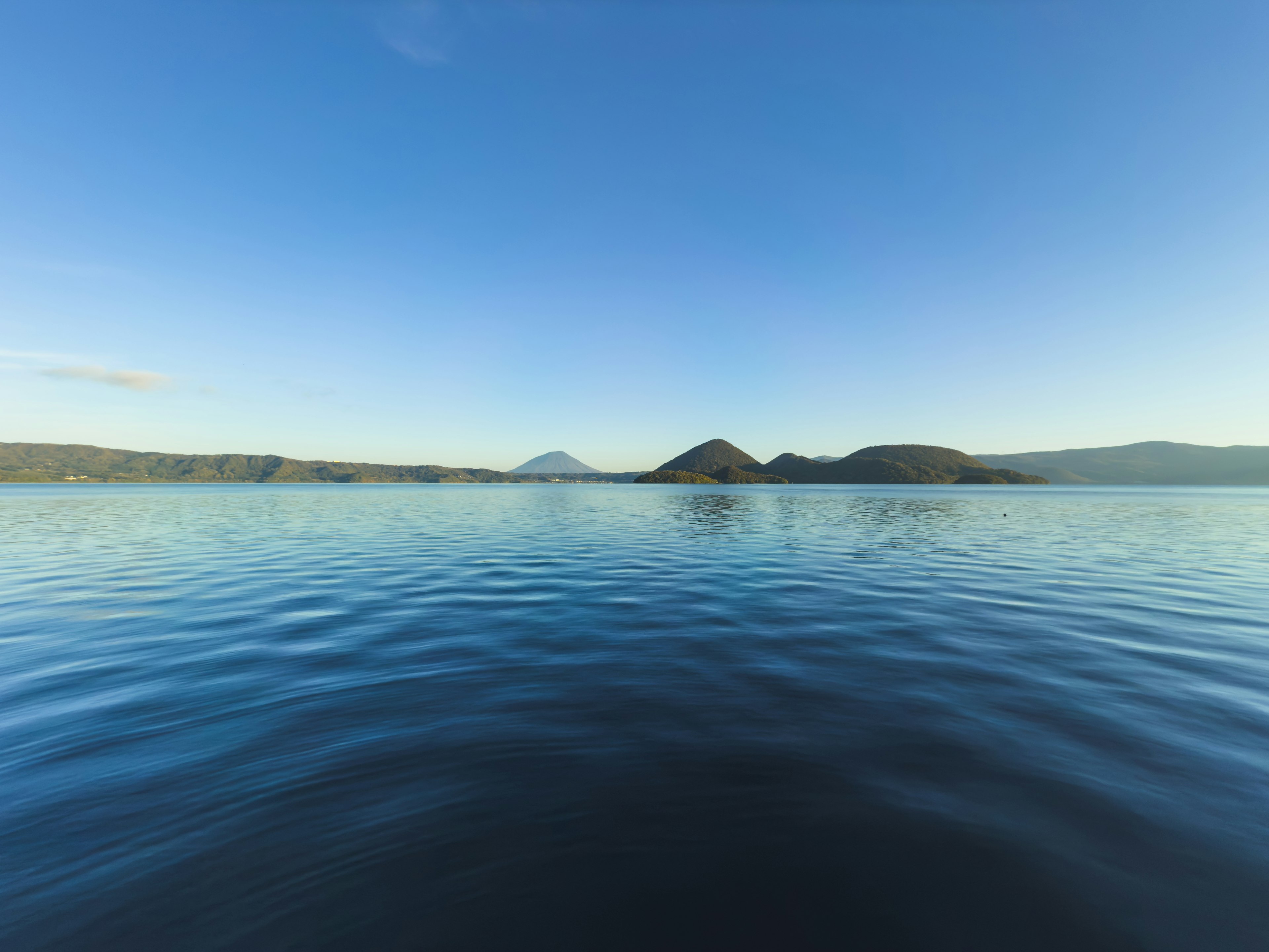 Surface de lac sereine avec un ciel bleu clair et des montagnes au loin