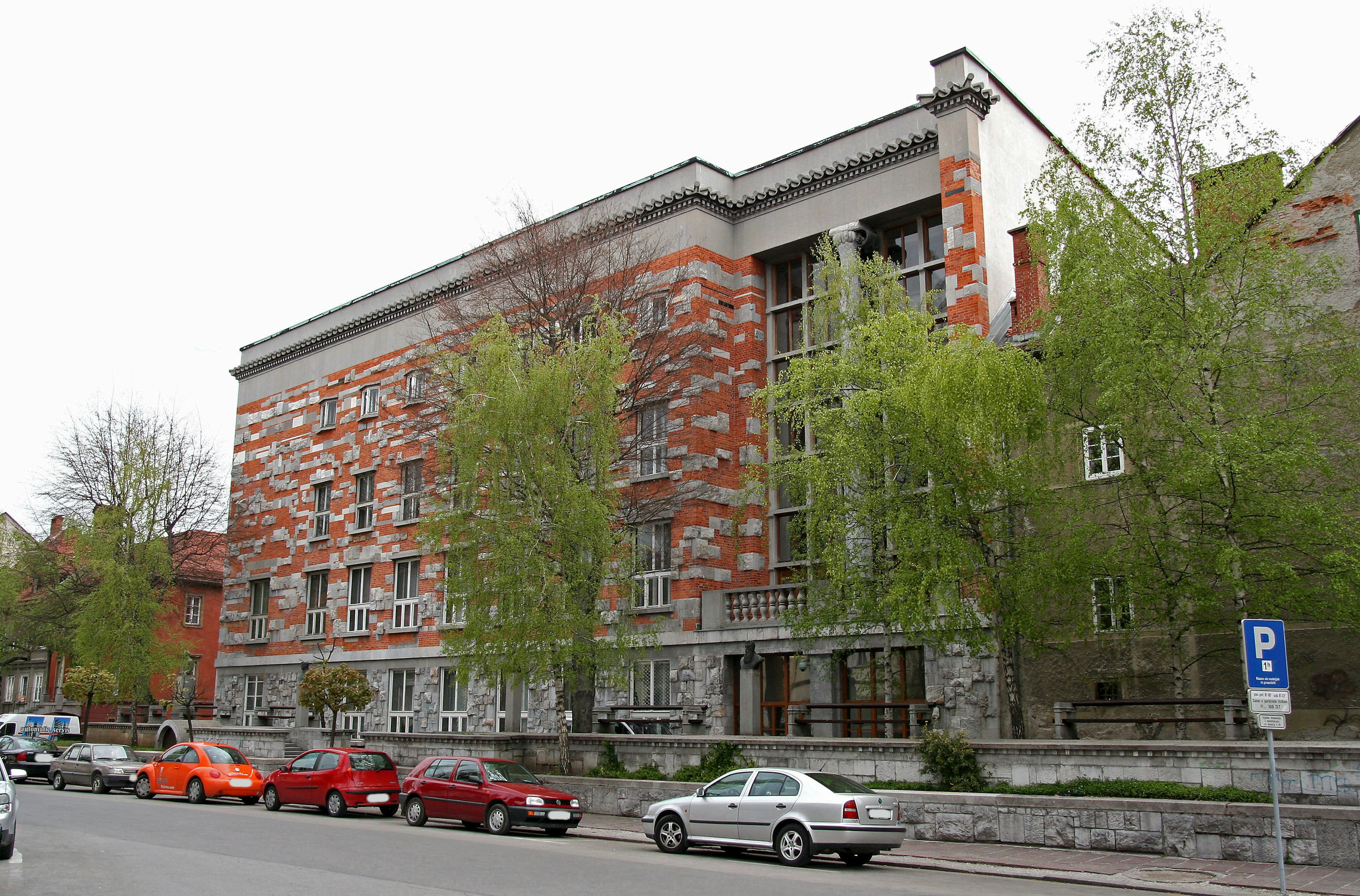 Bâtiment moderne avec une façade orange et grise, entouré d'arbres verts et d'un parking, paysage urbain