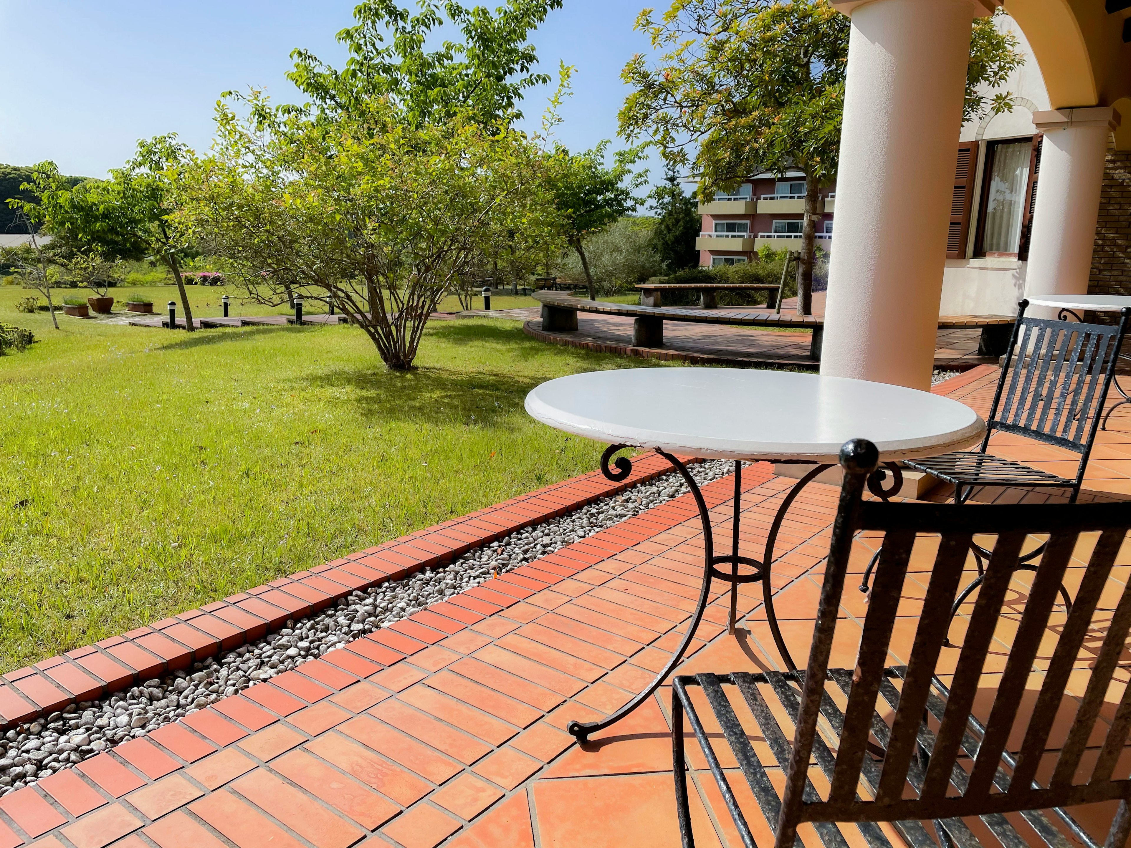 Una mesa blanca y una silla de hierro forjado en una terraza con vista a un hermoso jardín