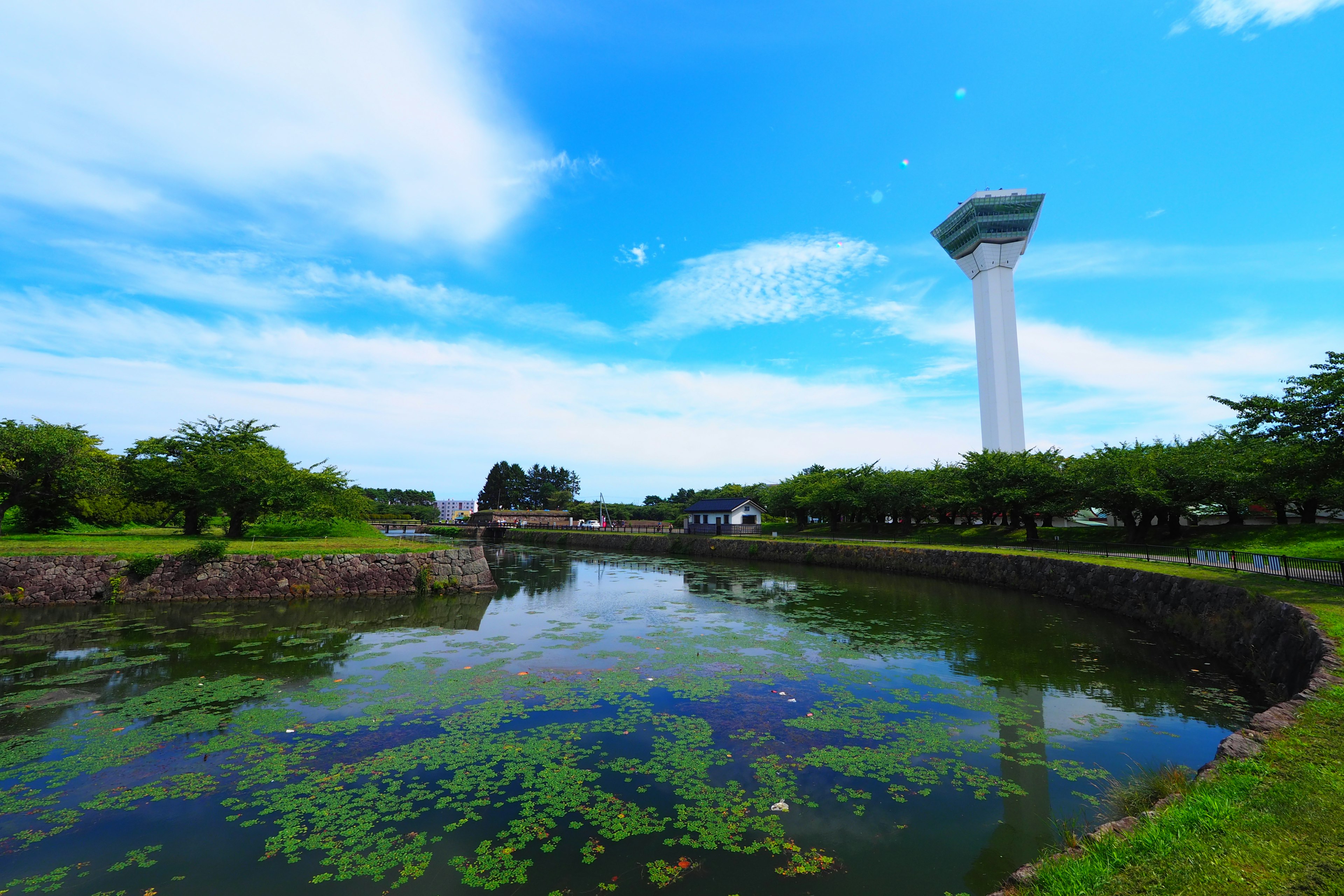 Tall tower against a blue sky with lush greenery and a reflective water surface