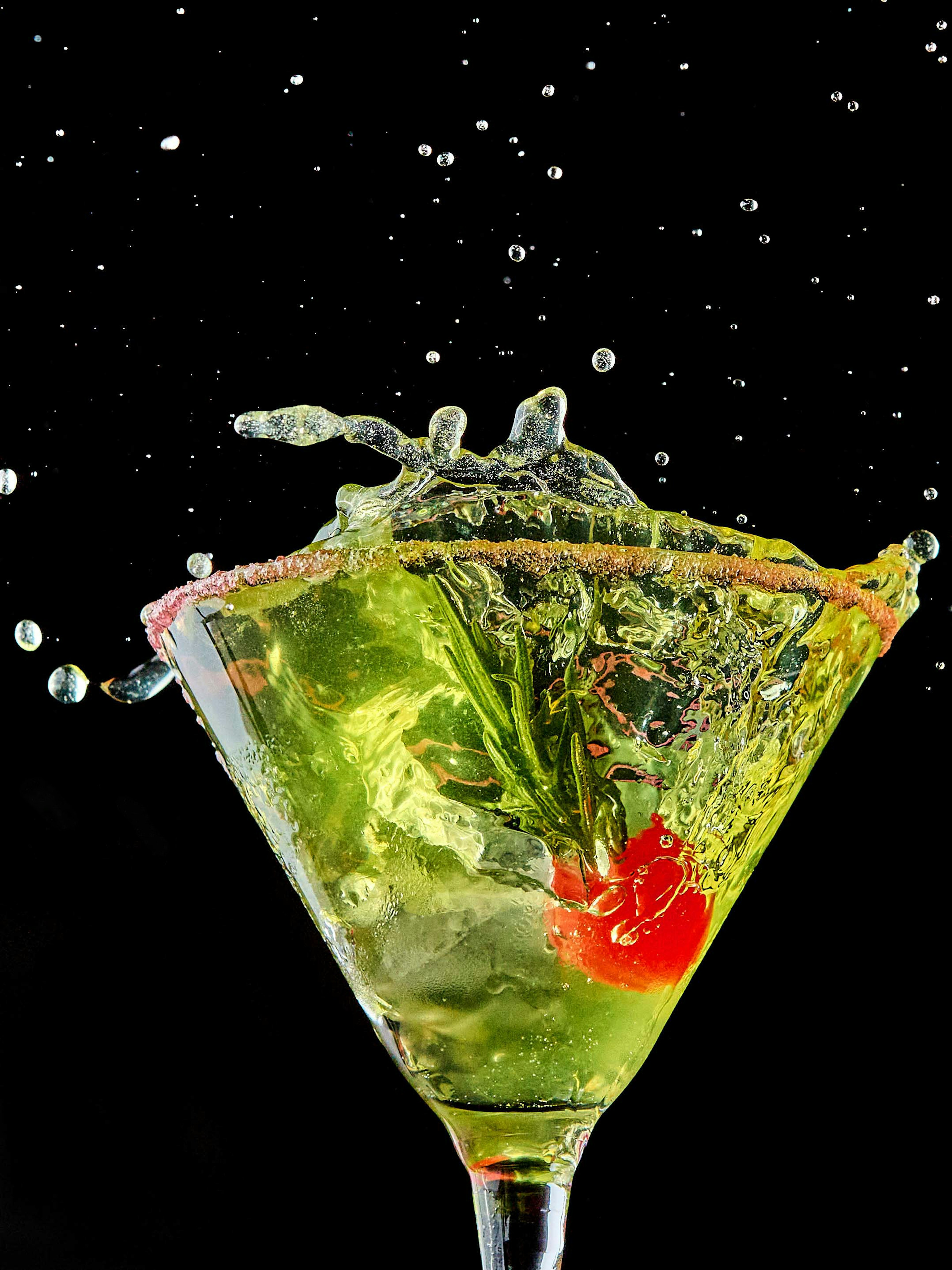 Cóctel verde vibrante con cereza salpicando de una copa de martini