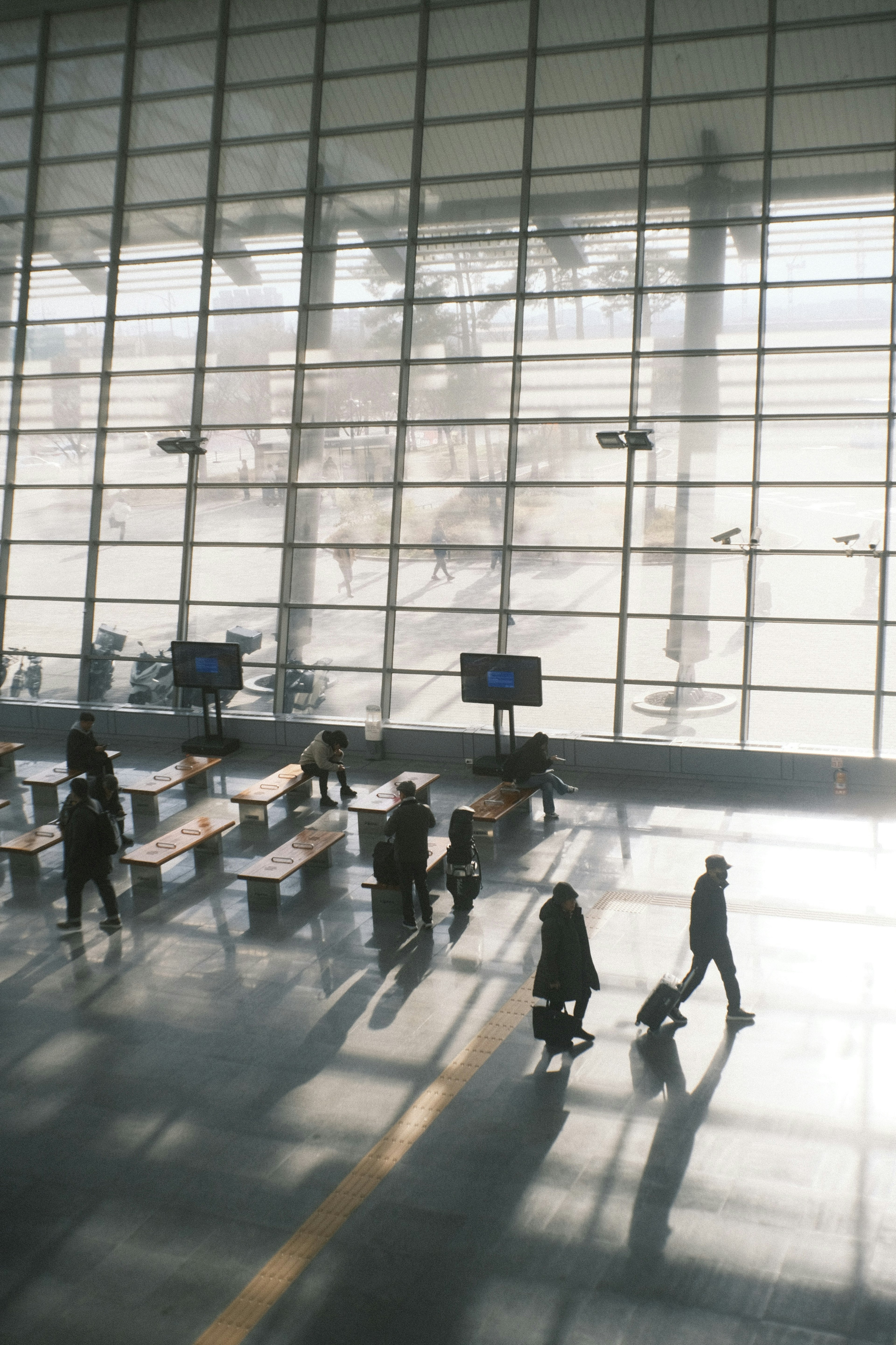 広い空港の待合室で人々が歩いているシルエットと大きな窓からの自然光