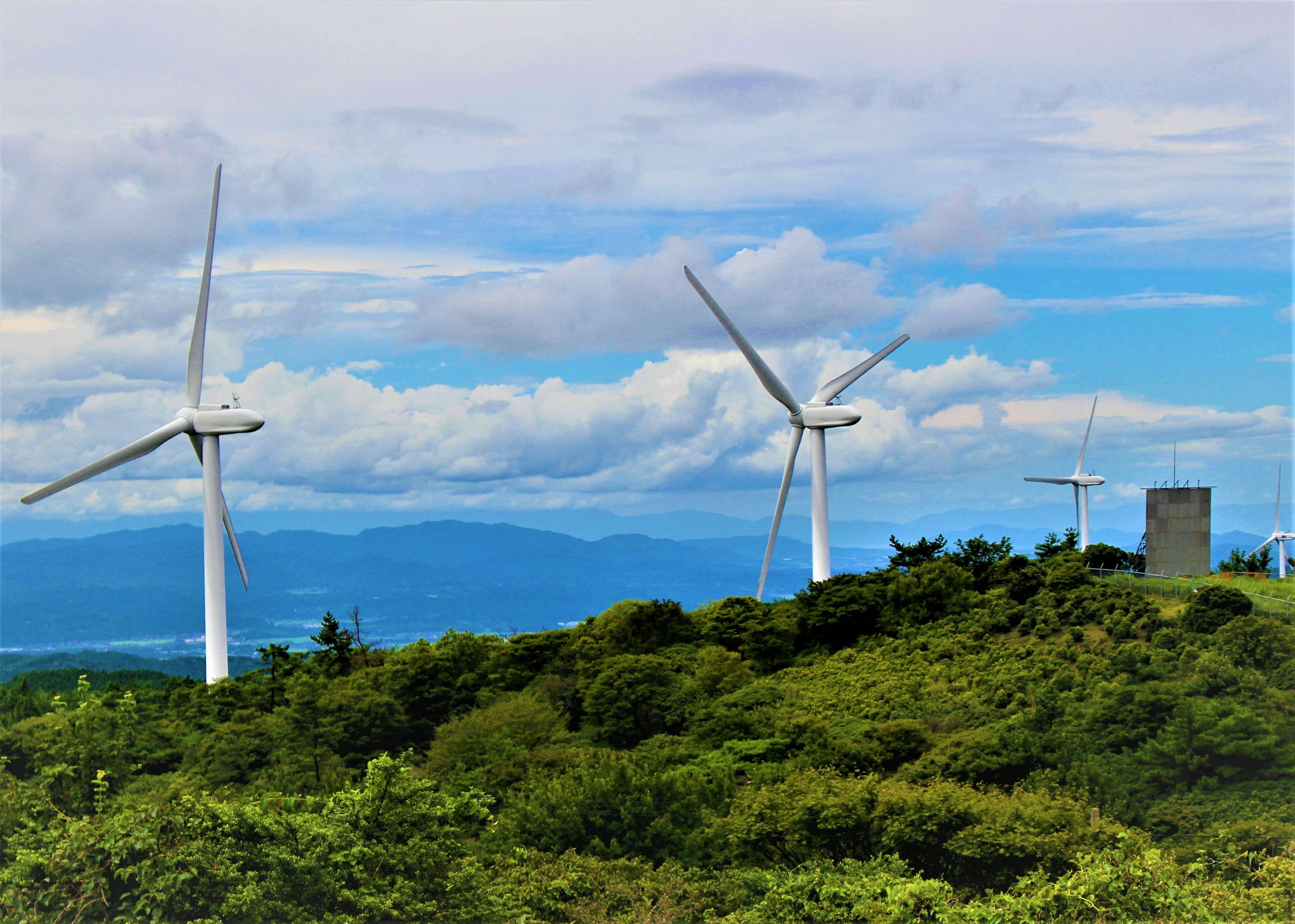 Landscape of wind turbines on a green hill with blue sky and clouds