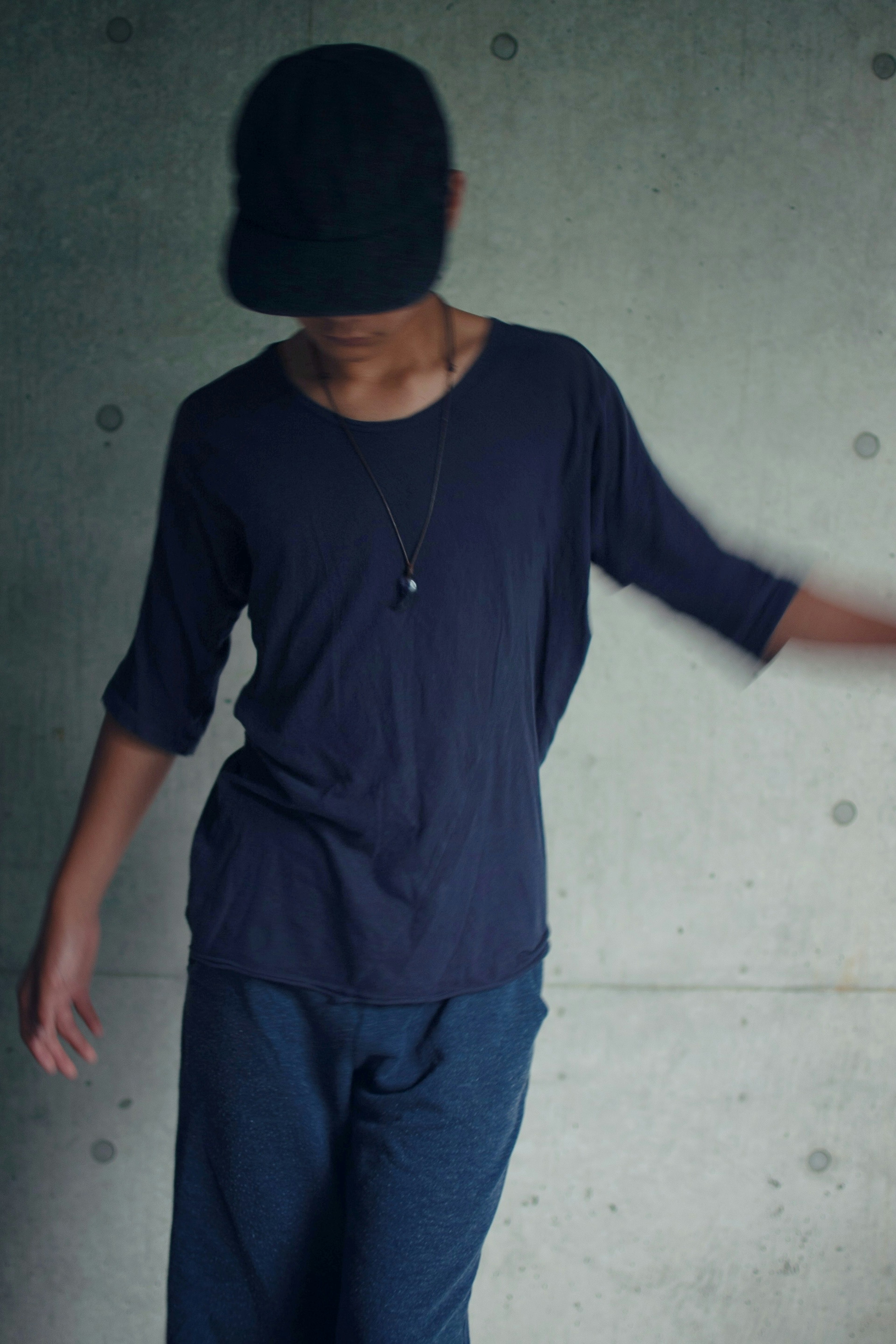 A boy wearing a dark-colored shirt and pants against a simple concrete wall