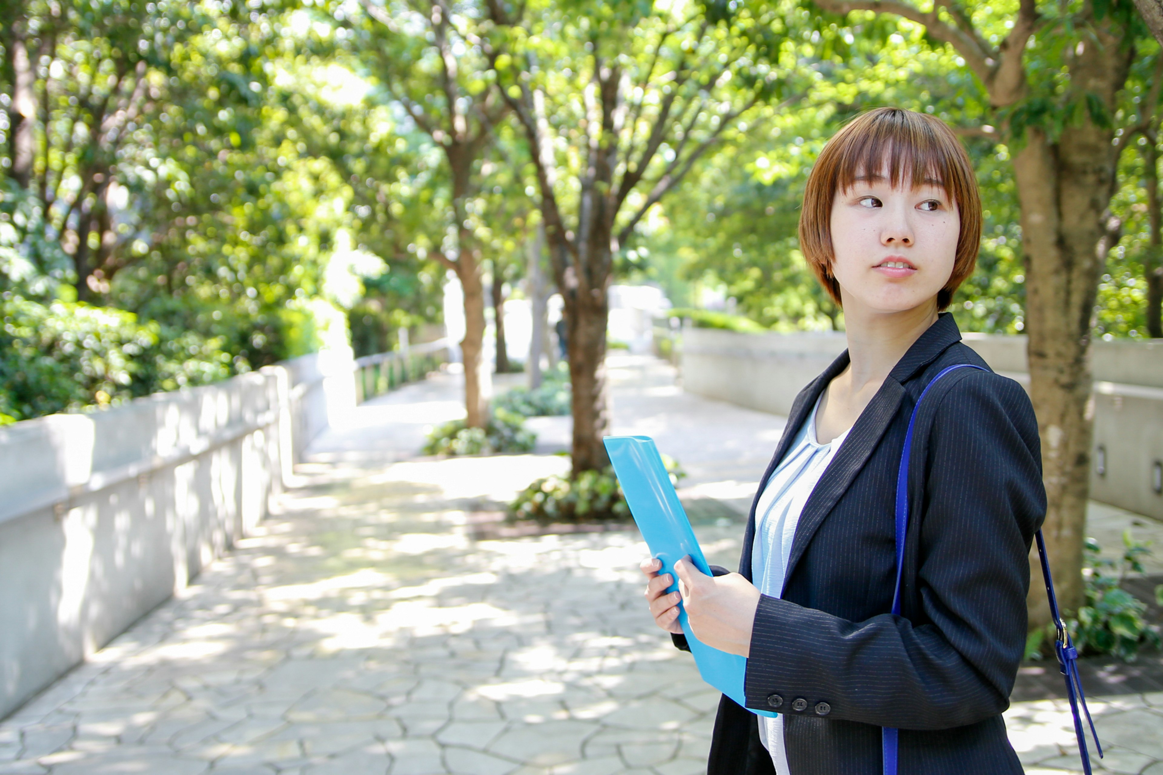 公園の中で青いファイルを持ち振り返る女性ビジネスパーソン