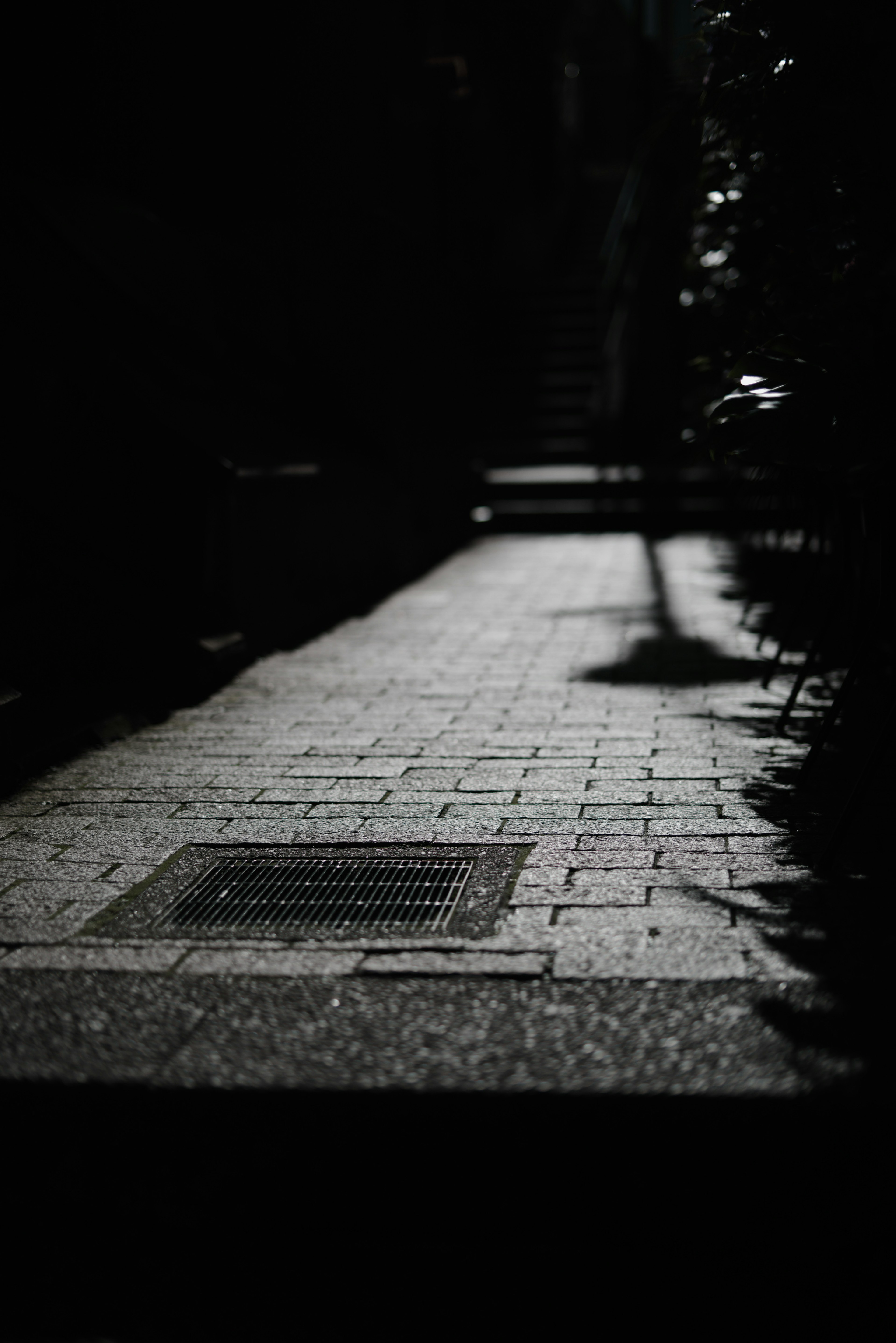 Dark pathway with tiled surface and drain cover in shadow