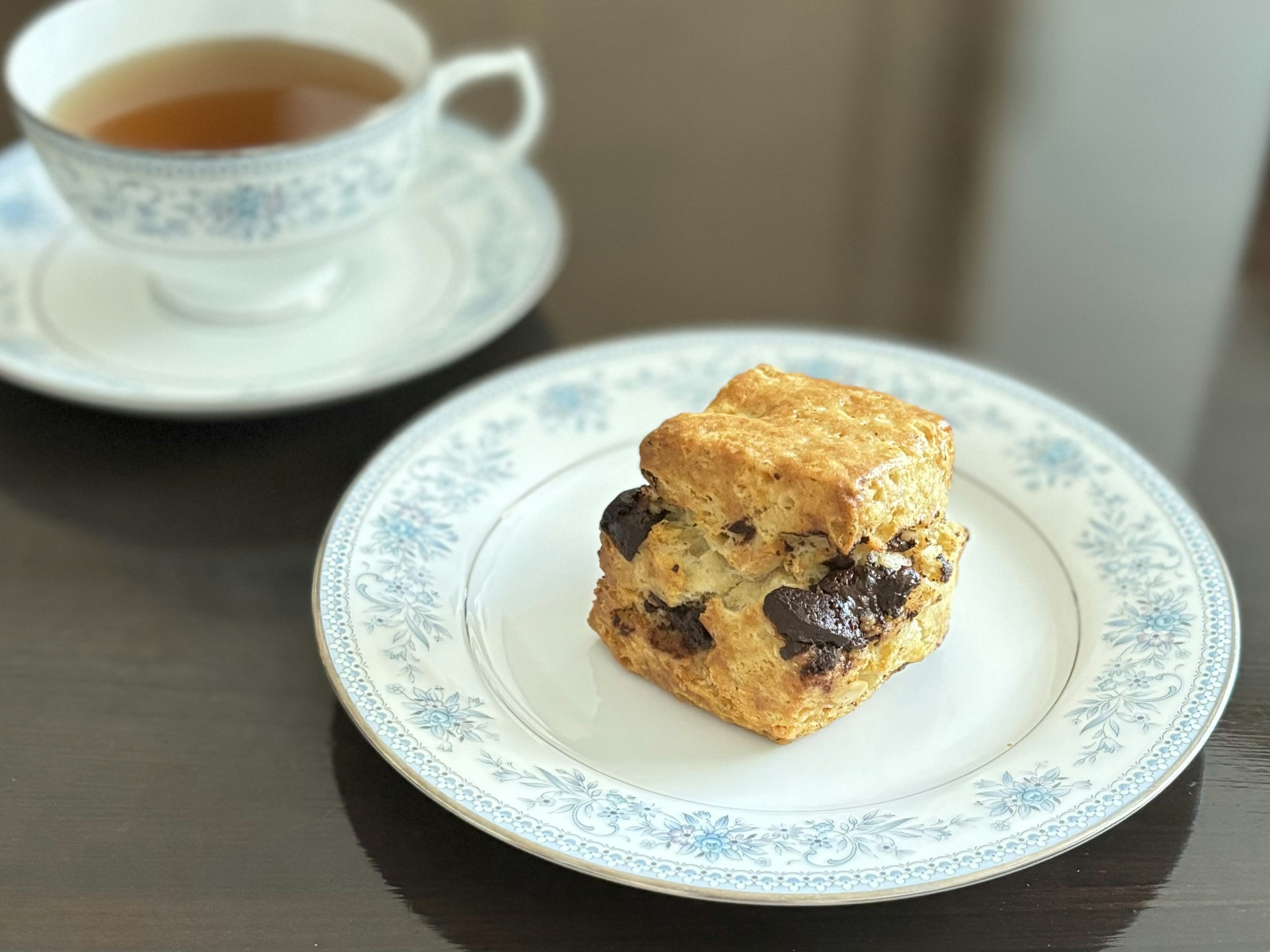 青い花模様の皿の上に置かれたチョコチップスコーンと紅茶