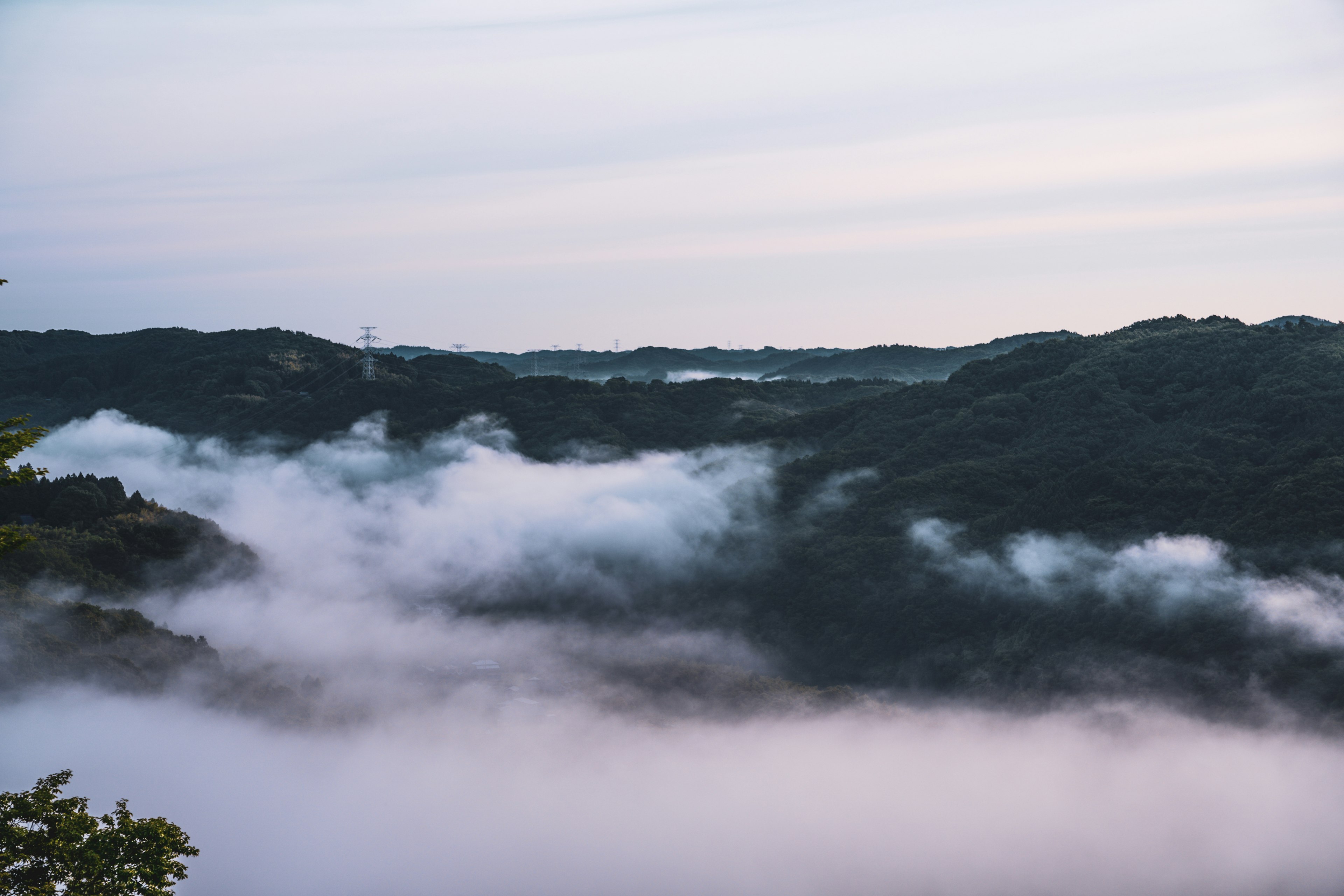 Berglandschaft, die von Nebel bedeckt ist, mit sanften Farbtönen im Himmel