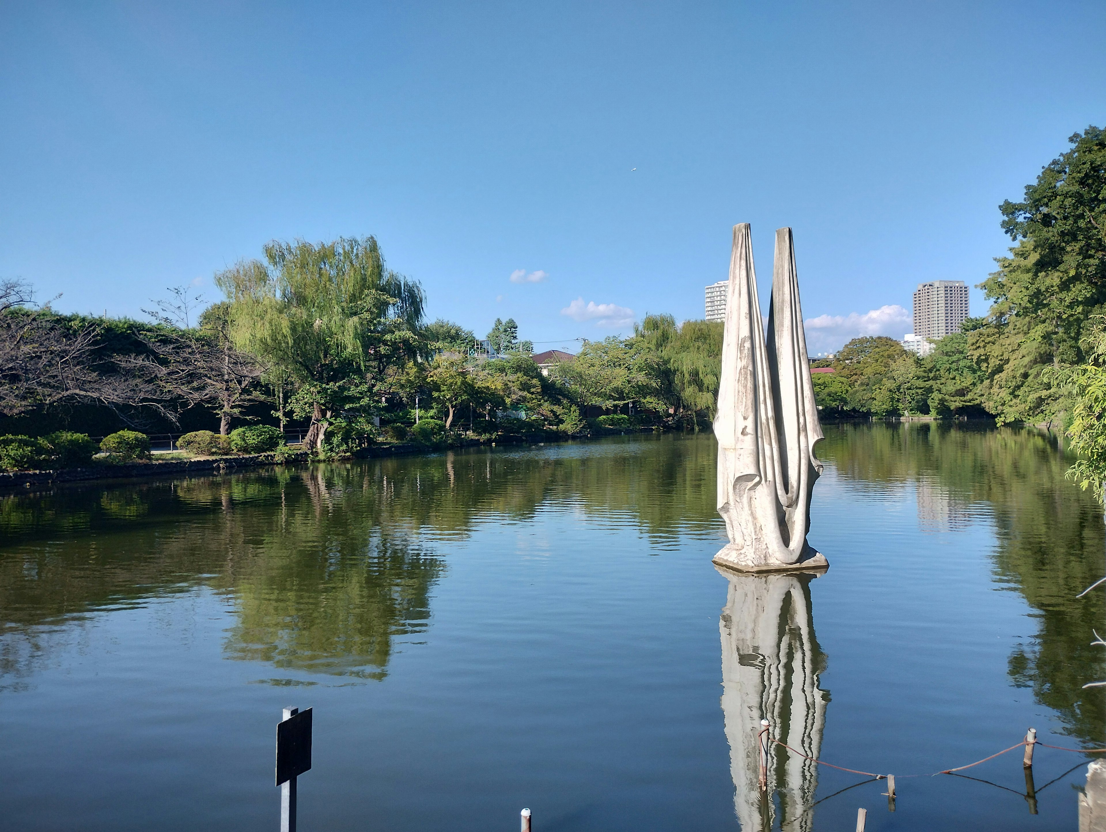 Stagno sereno con vegetazione lussureggiante e scultura che si riflette nell'acqua