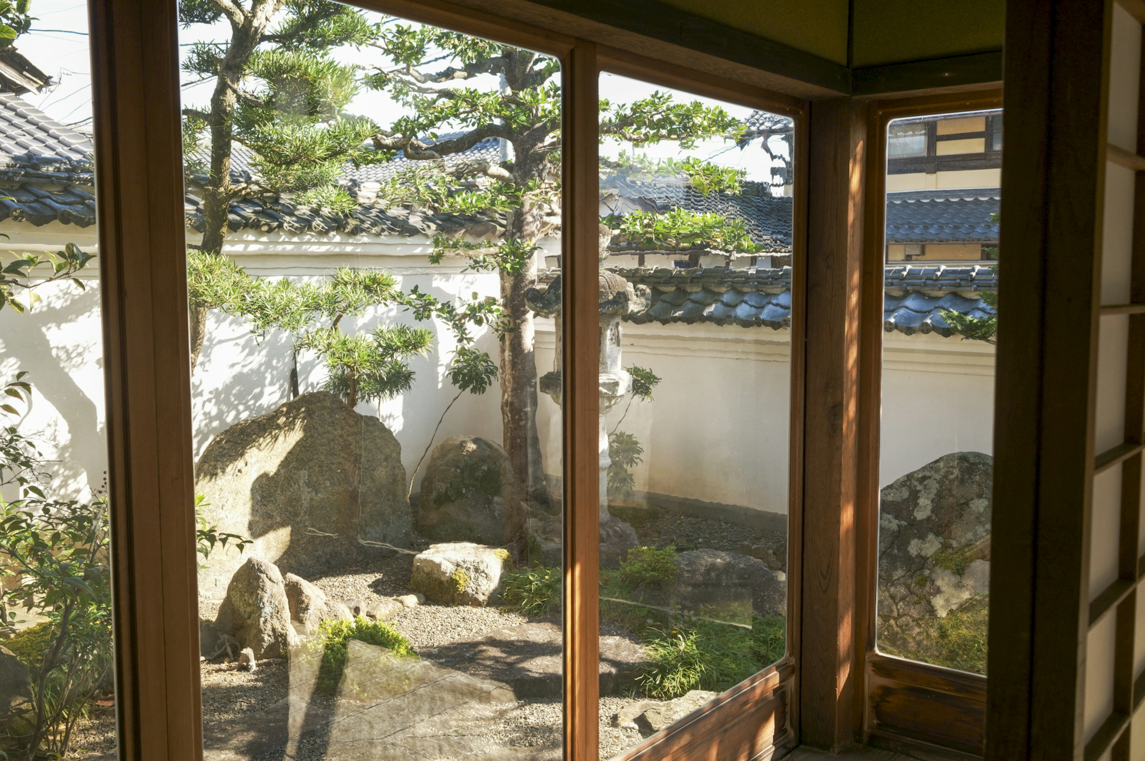 Vista de un hermoso jardín japonés a través de ventanas de madera con pinos verdes y piedras