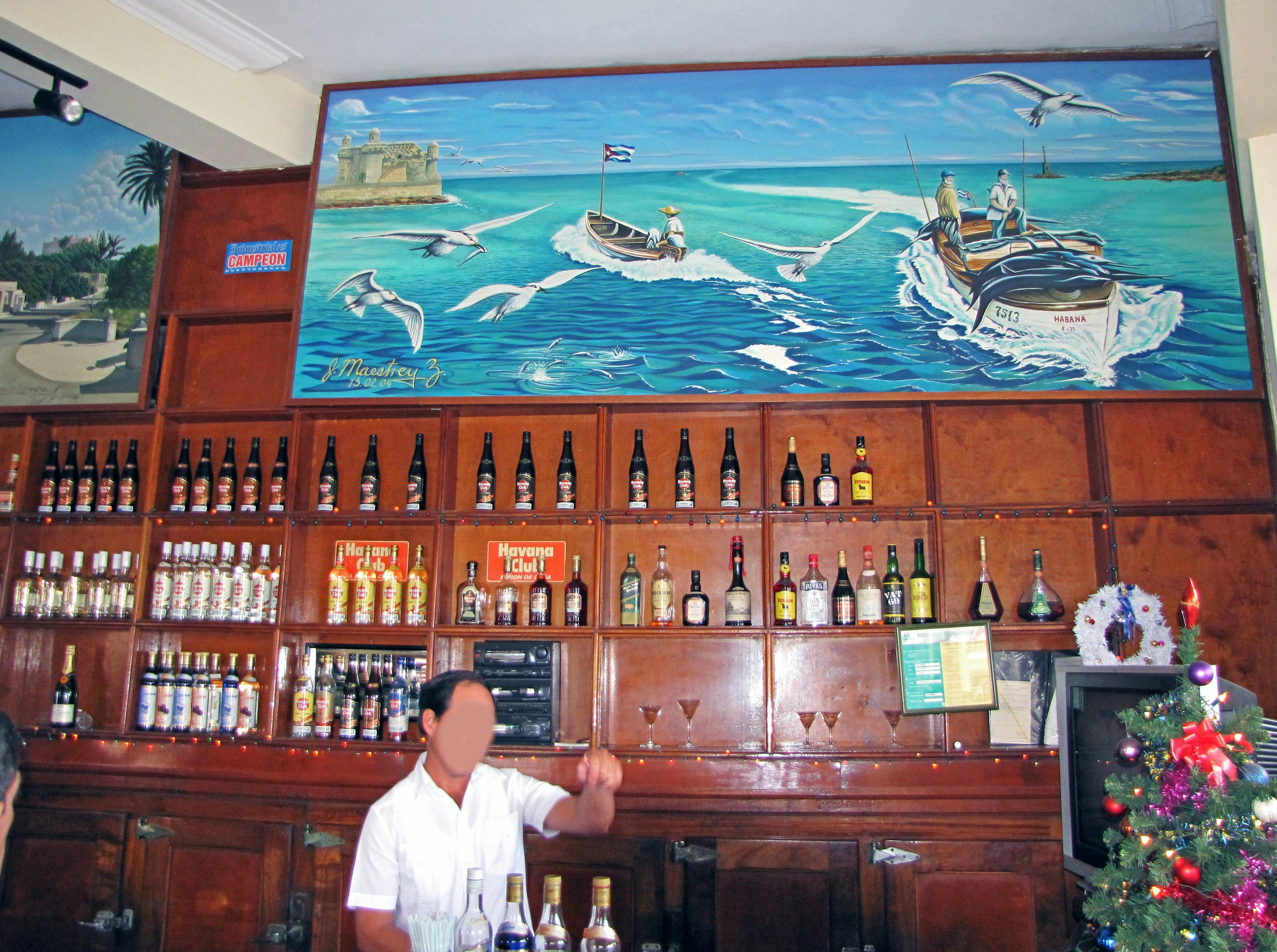 Interior bar dengan mural pemandangan laut dan meja penuh botol