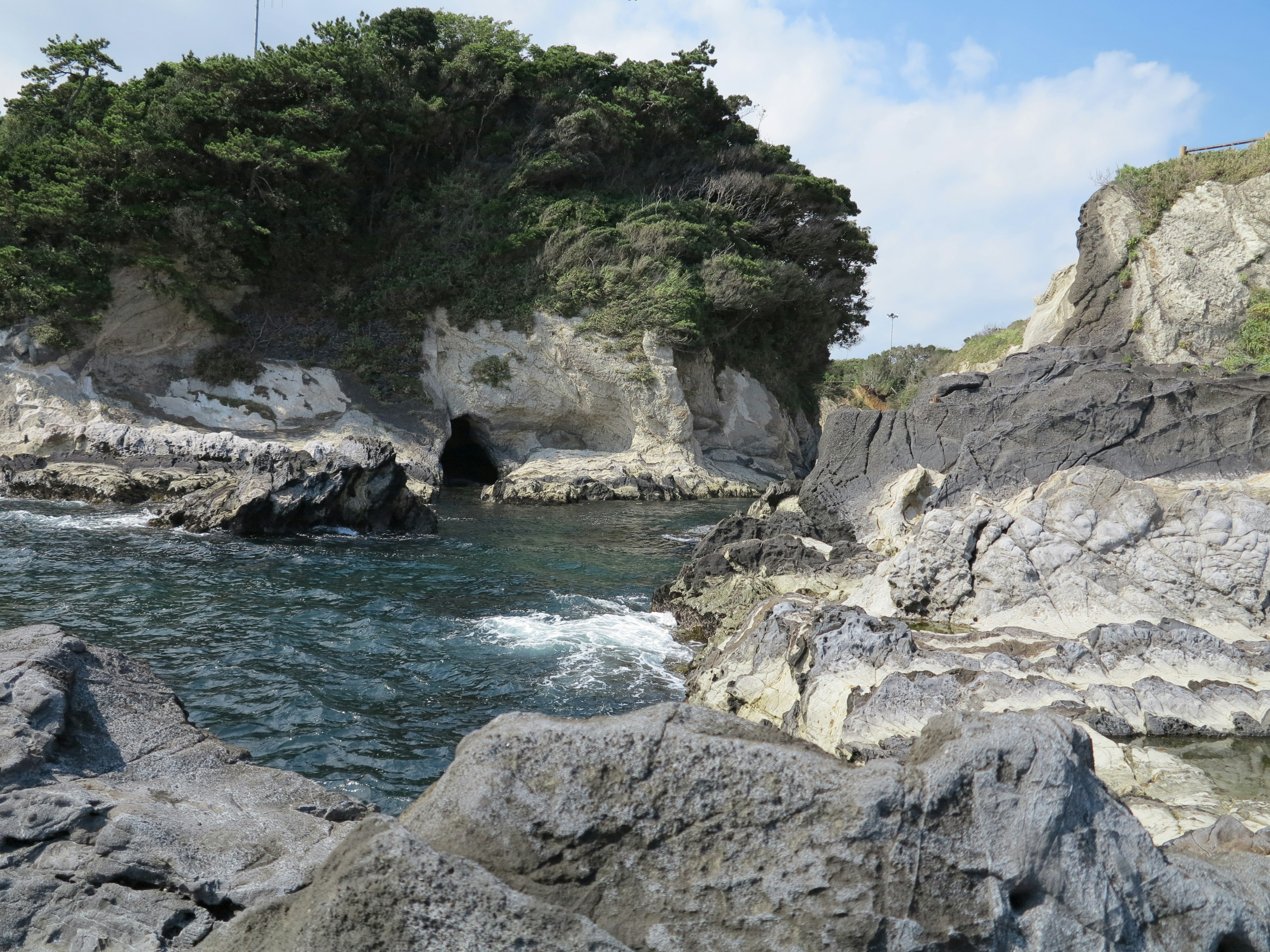 Pemandangan pantai dengan formasi batu dan pepohonan hijau