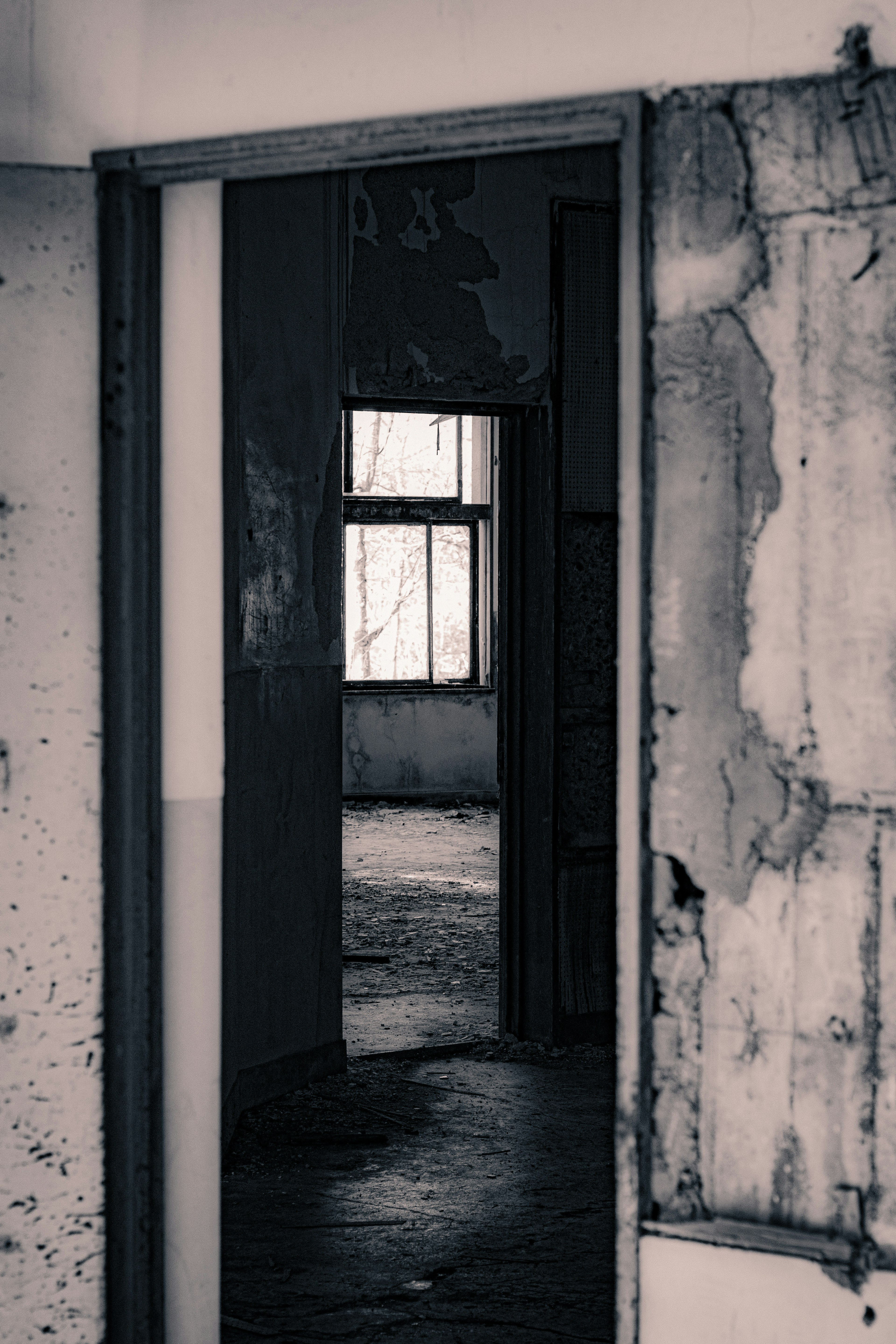 View through an old doorway into a dimly lit room with peeling walls and a window