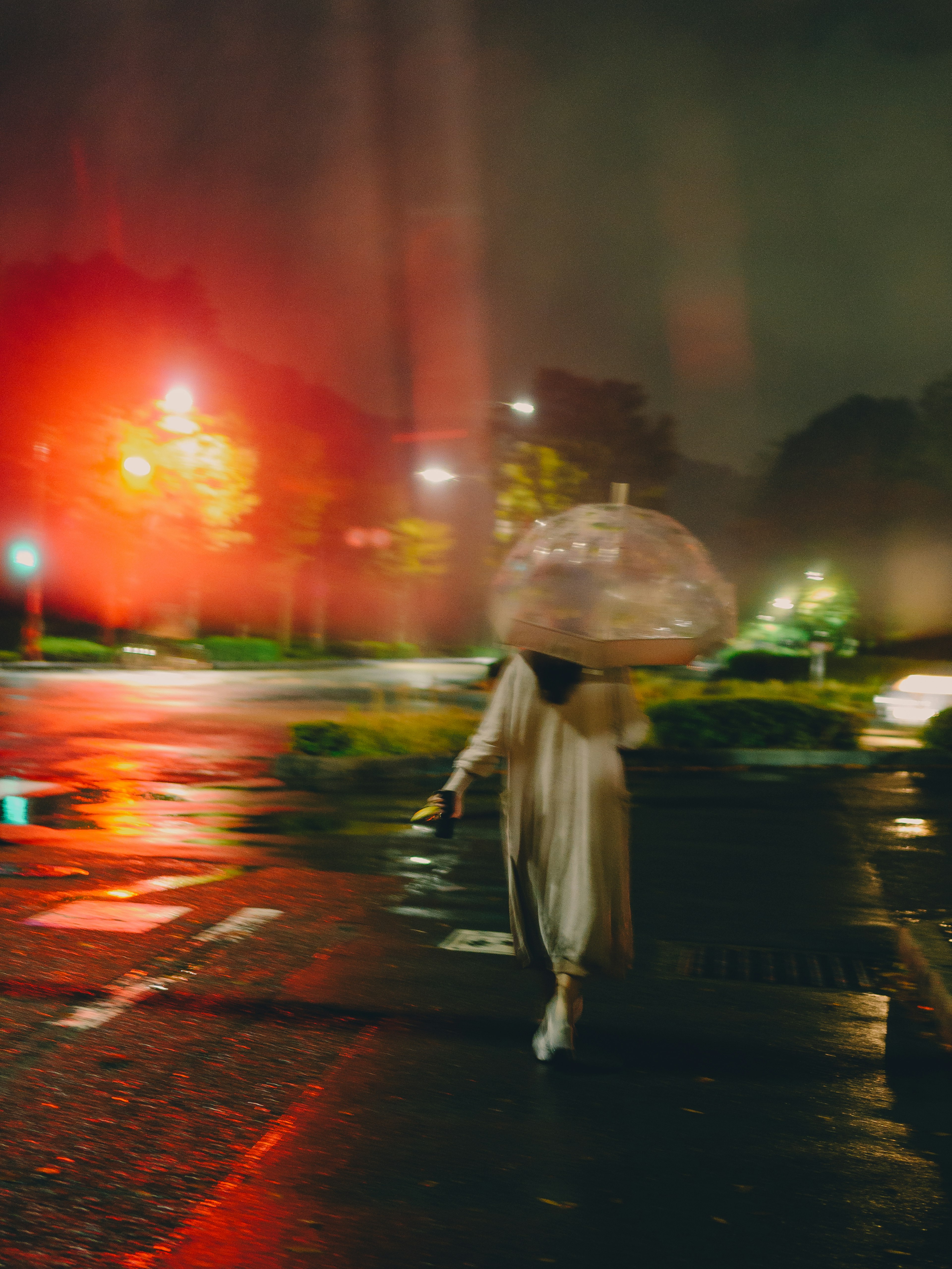 A person walking in the night holding a transparent umbrella amidst fog and rain with red lights