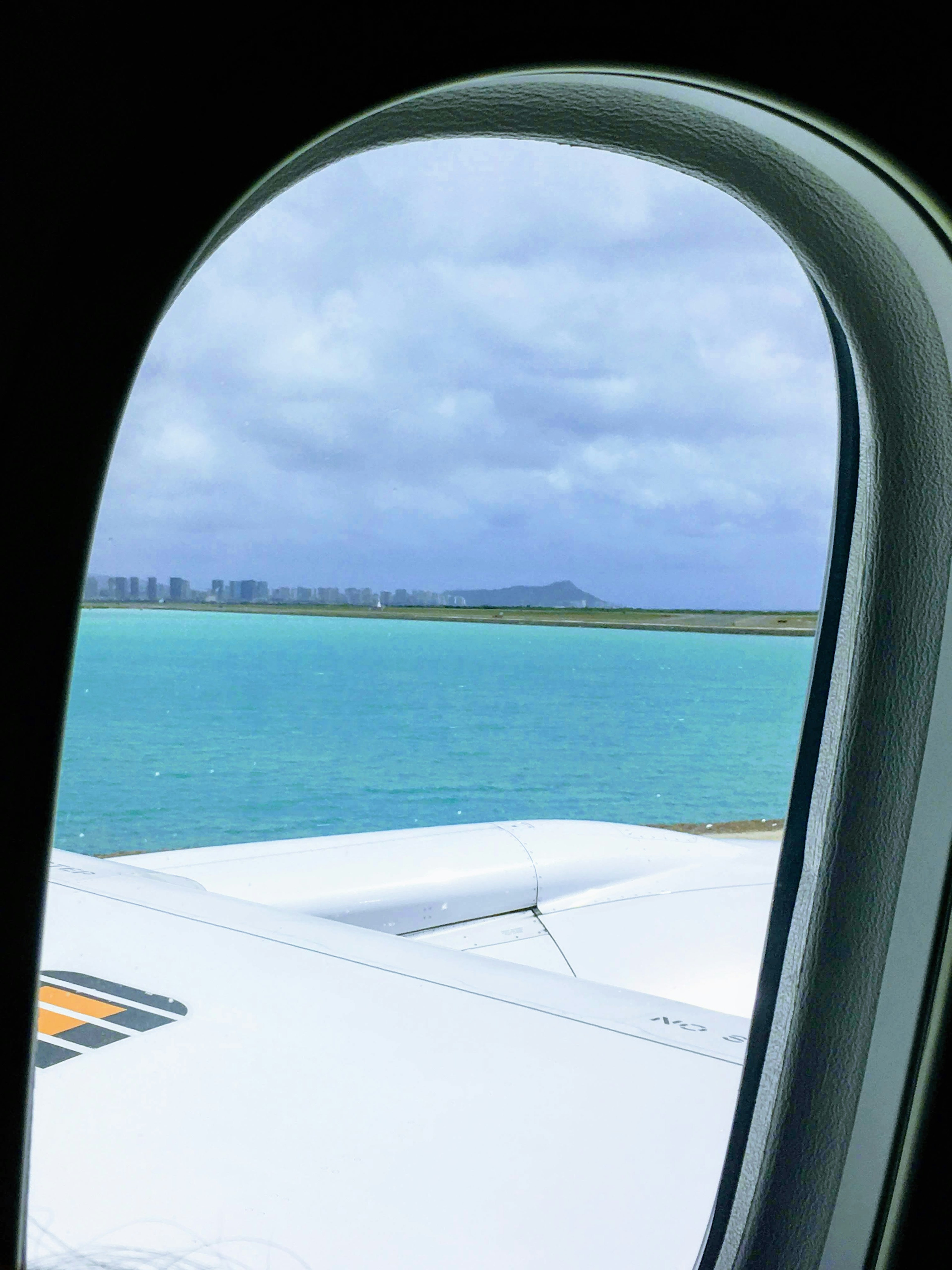 飛行機の窓から見える青い海と雲のある空