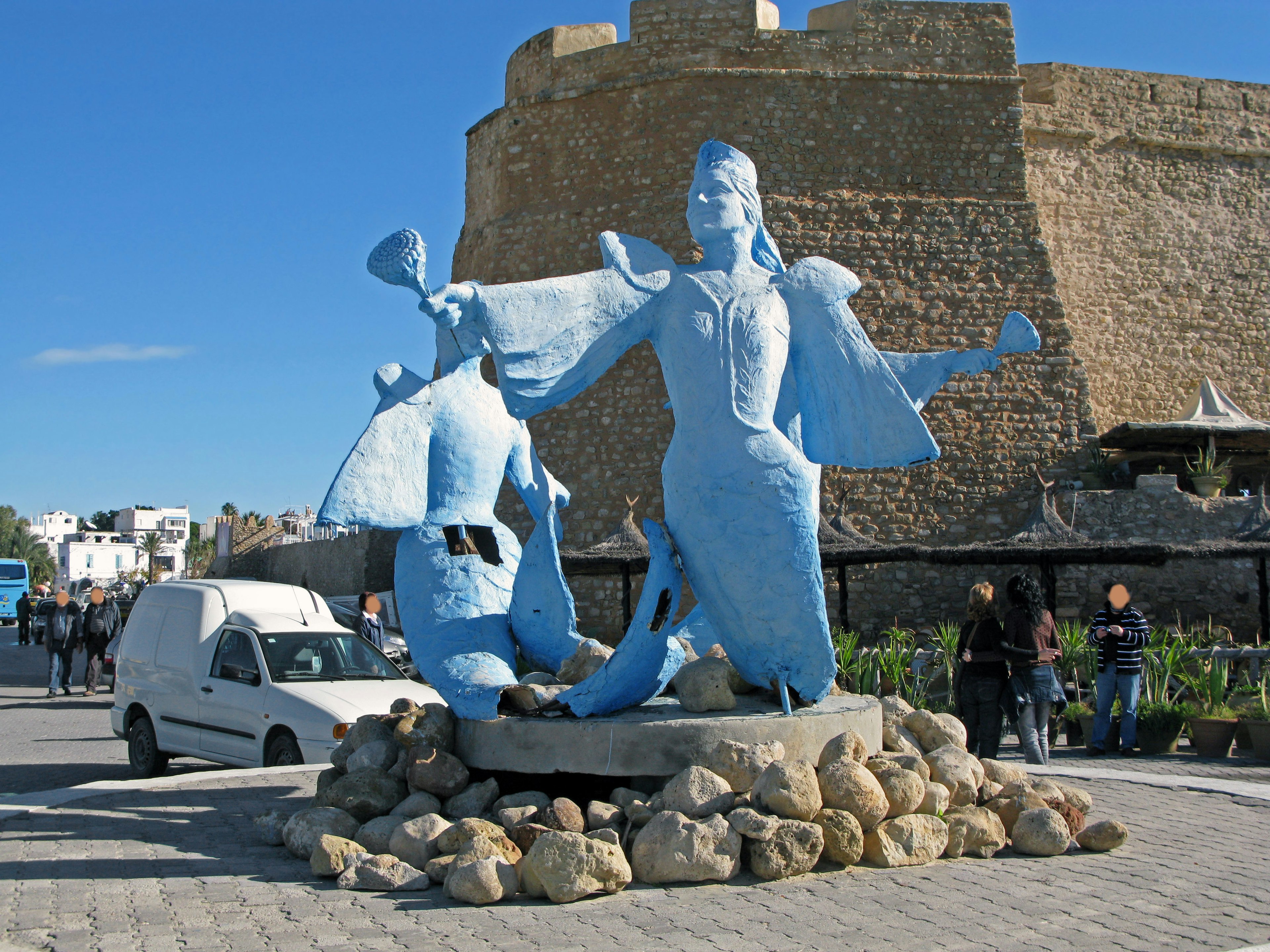 A blue sculpture in a square with a castle wall in the background