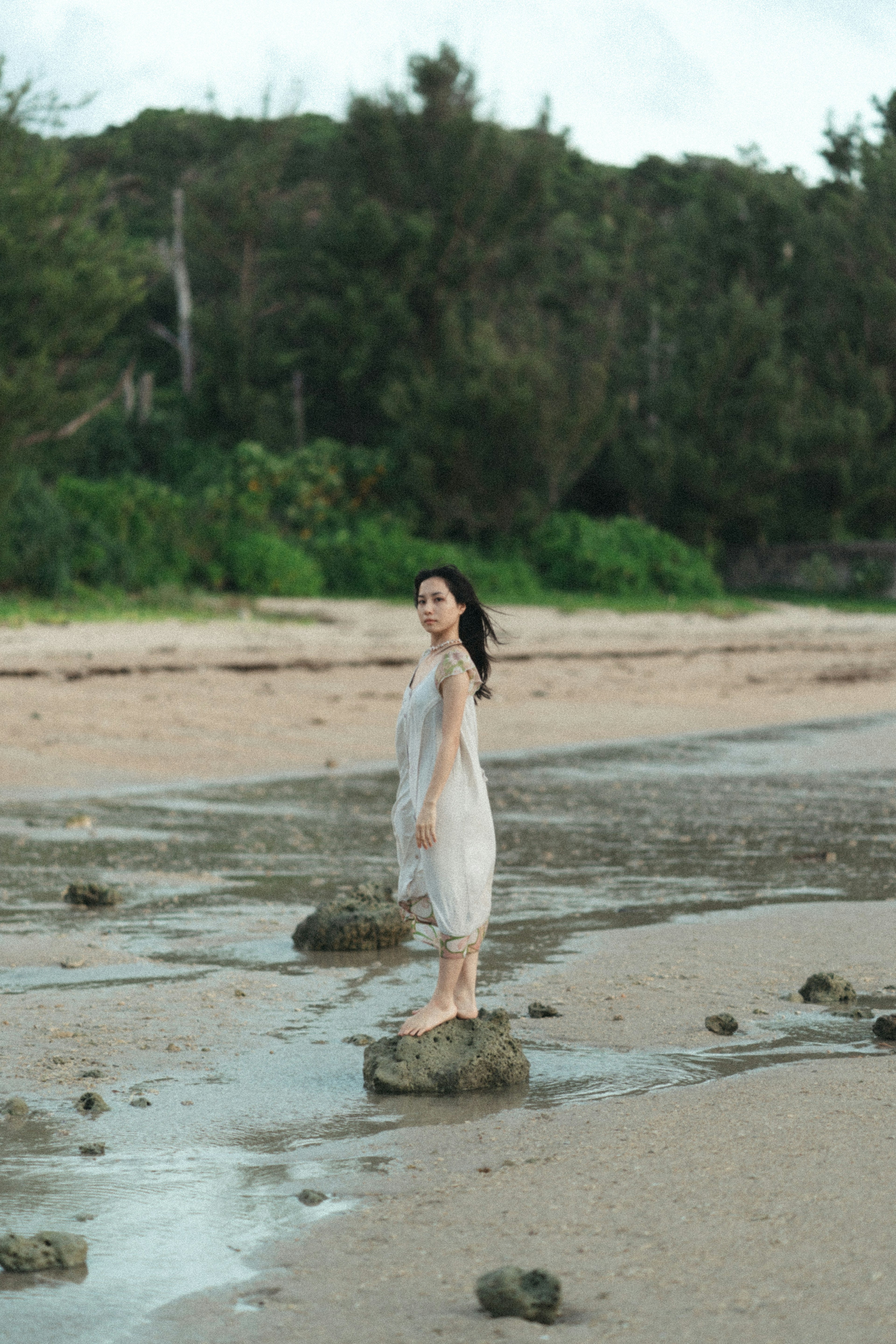 Wanita berdiri di atas batu di pantai dikelilingi alam