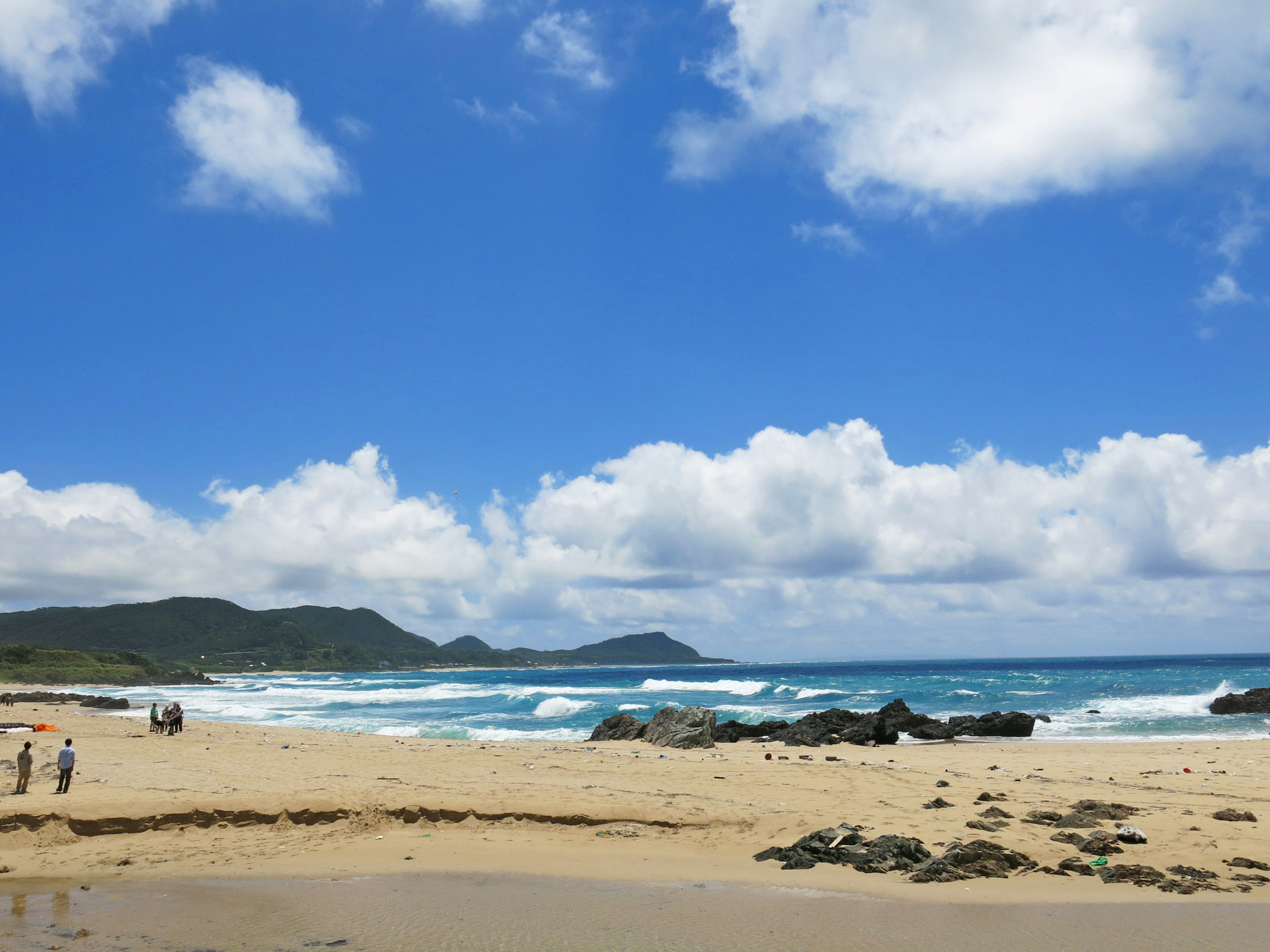 Strandszene mit blauem Himmel und weißen Wolken mit Menschen, die gehen