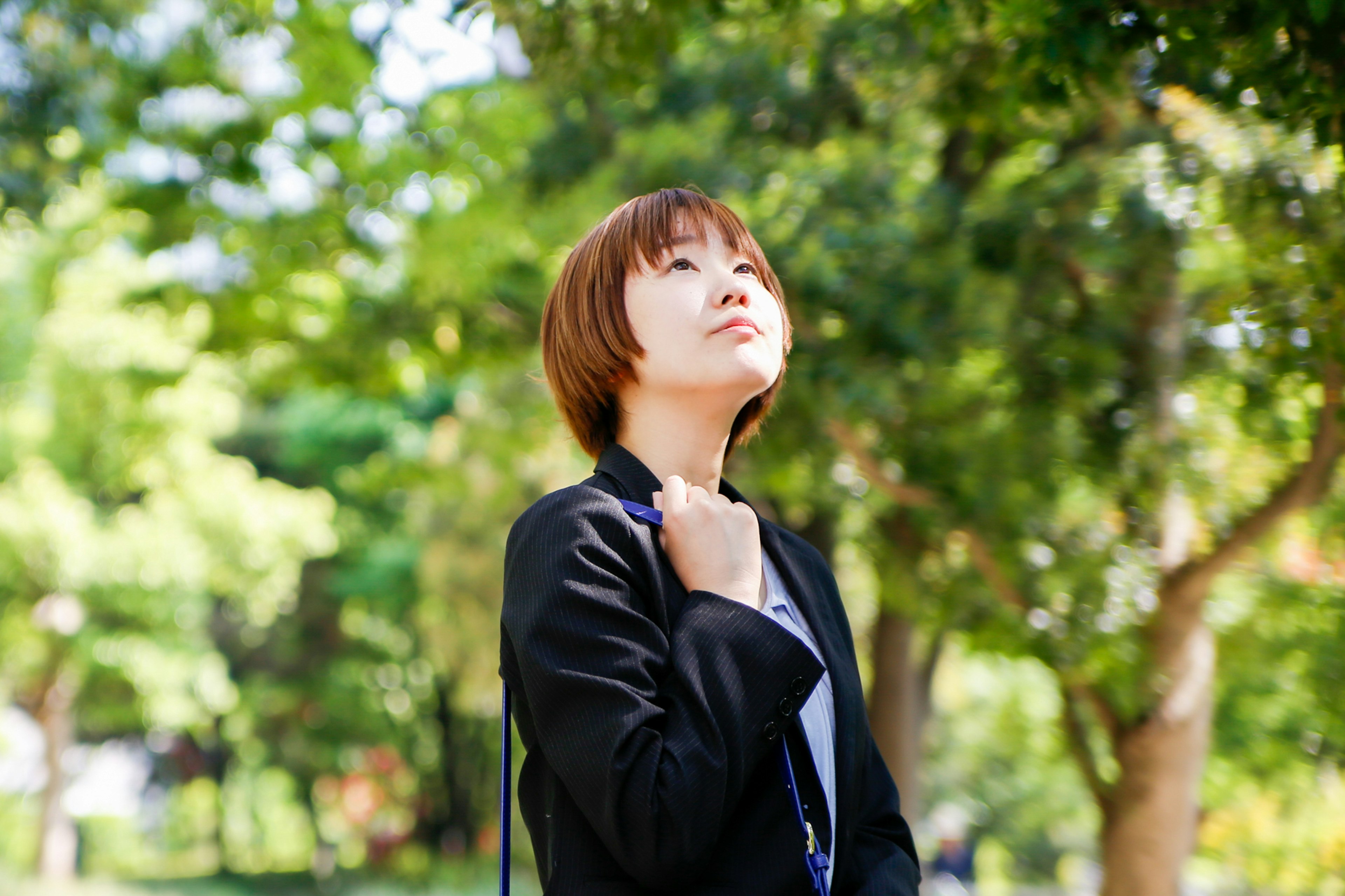 公園裡一位女性仰望天空的肖像，四周被綠色樹木環繞