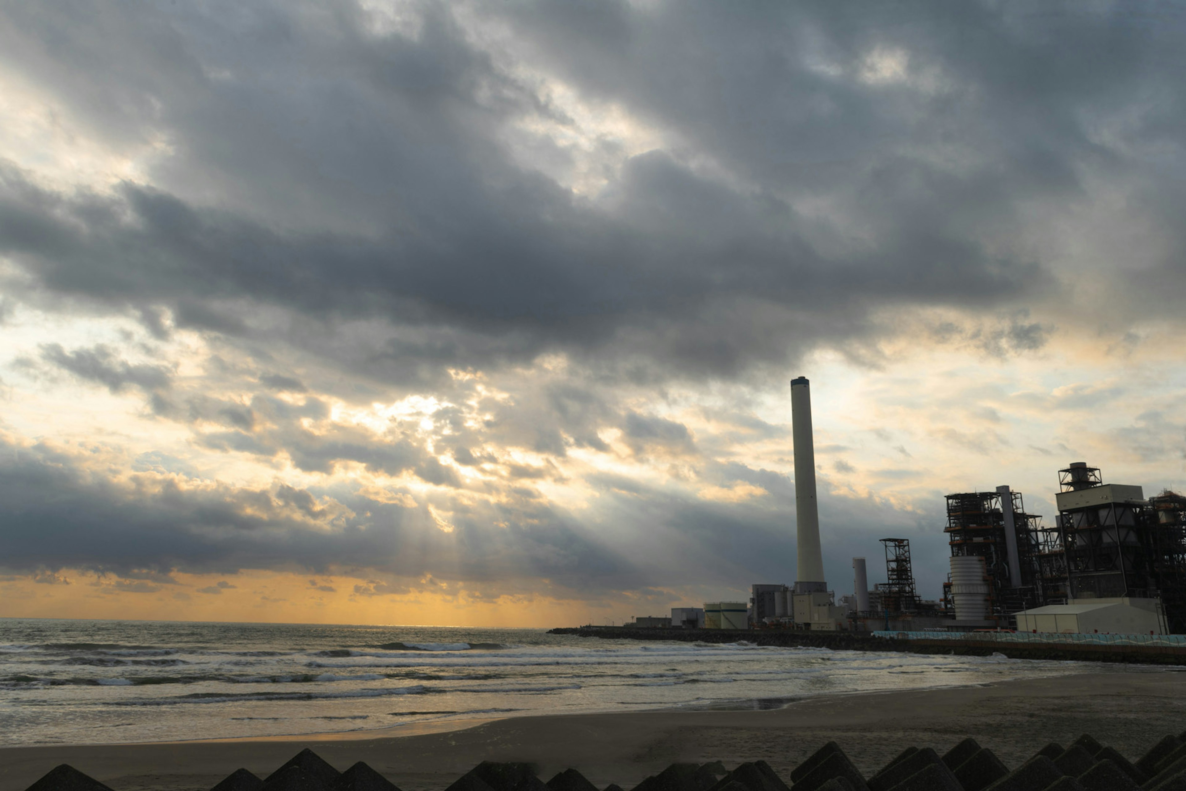 Strandansicht mit Fabrikschornstein bei Sonnenuntergang