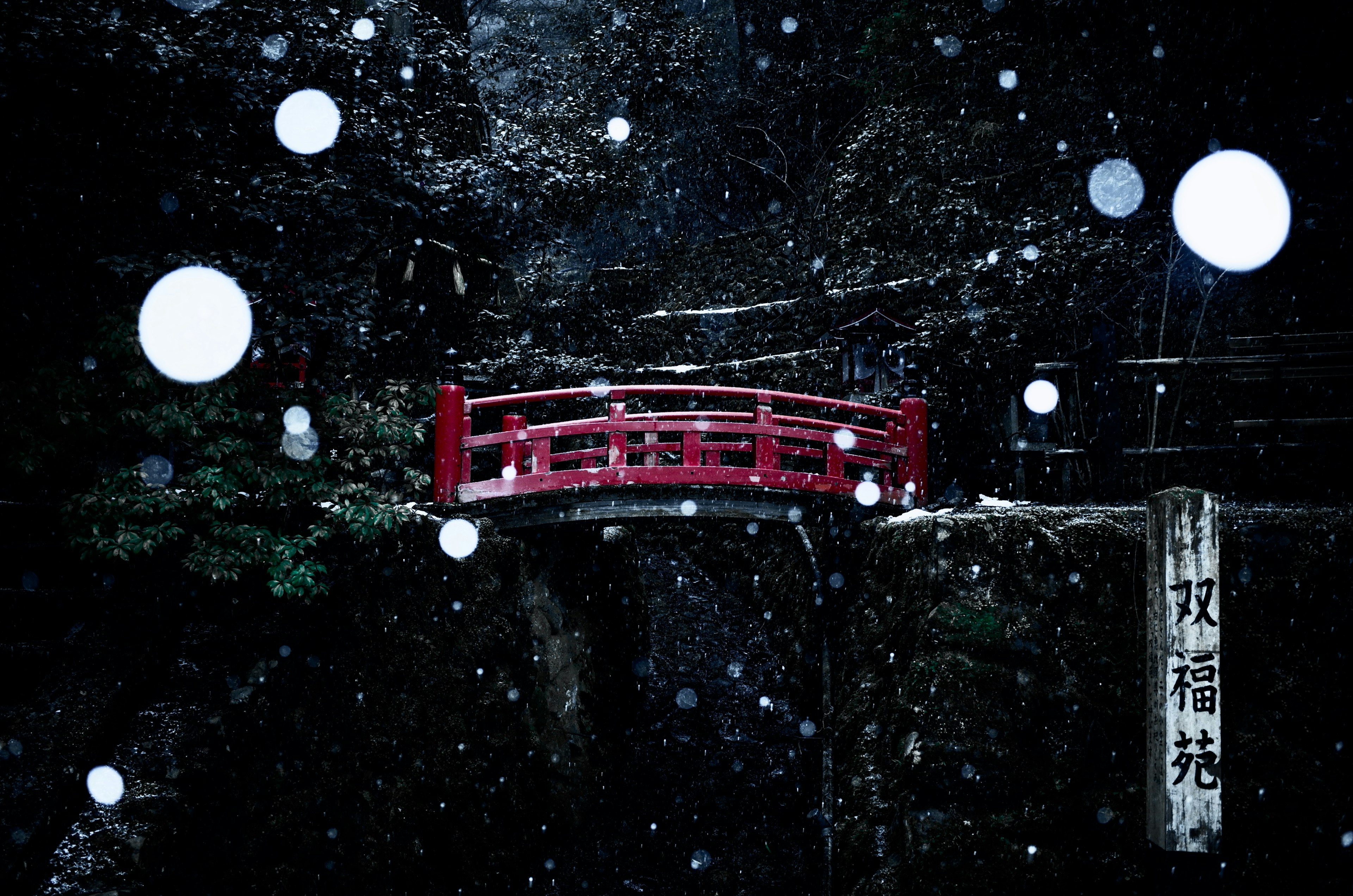 雪の中の赤い橋と周囲の暗い風景