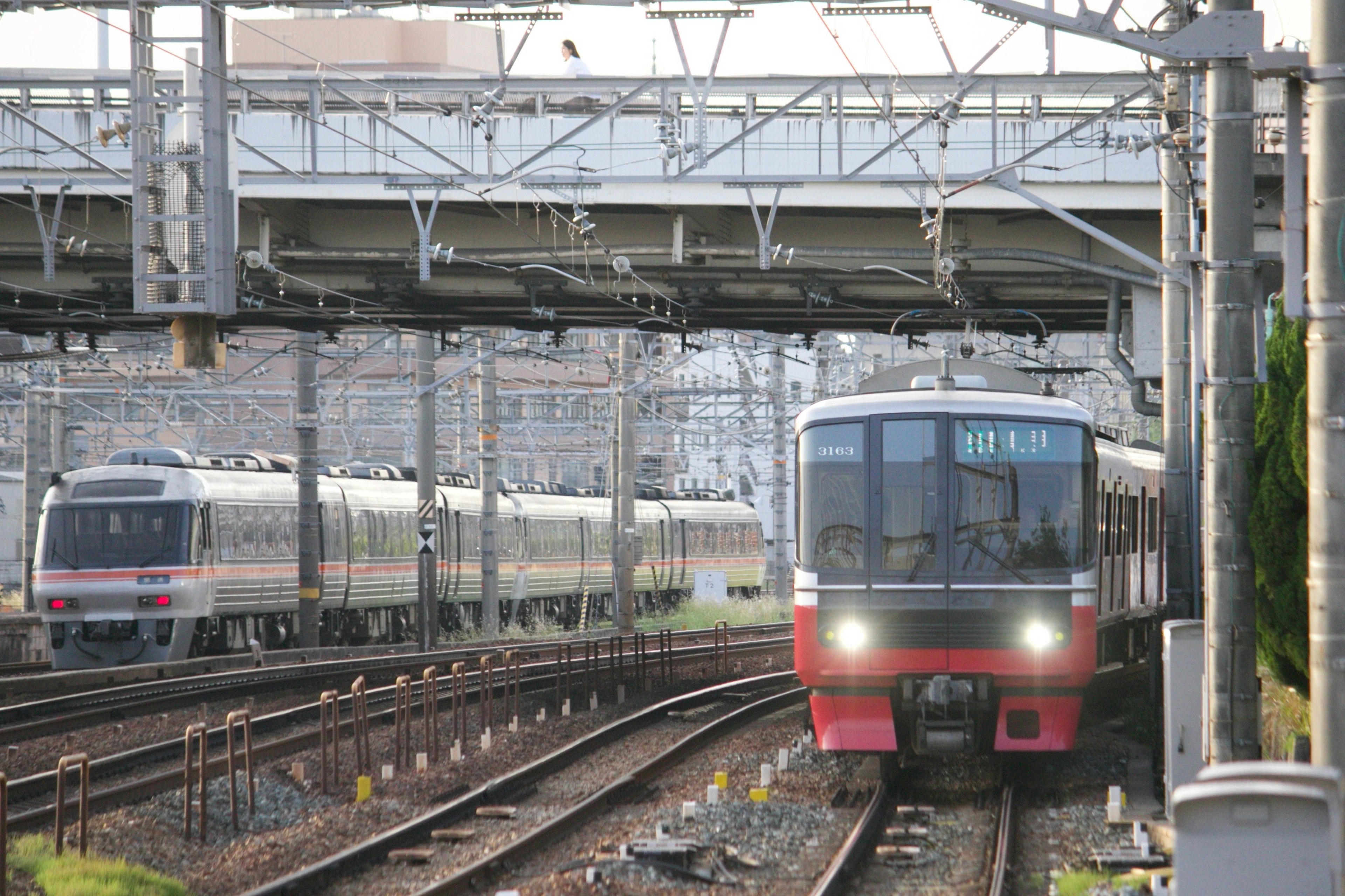 鉄道の線路上にいる二つの列車の画像、手前の列車は赤い前面を持つ