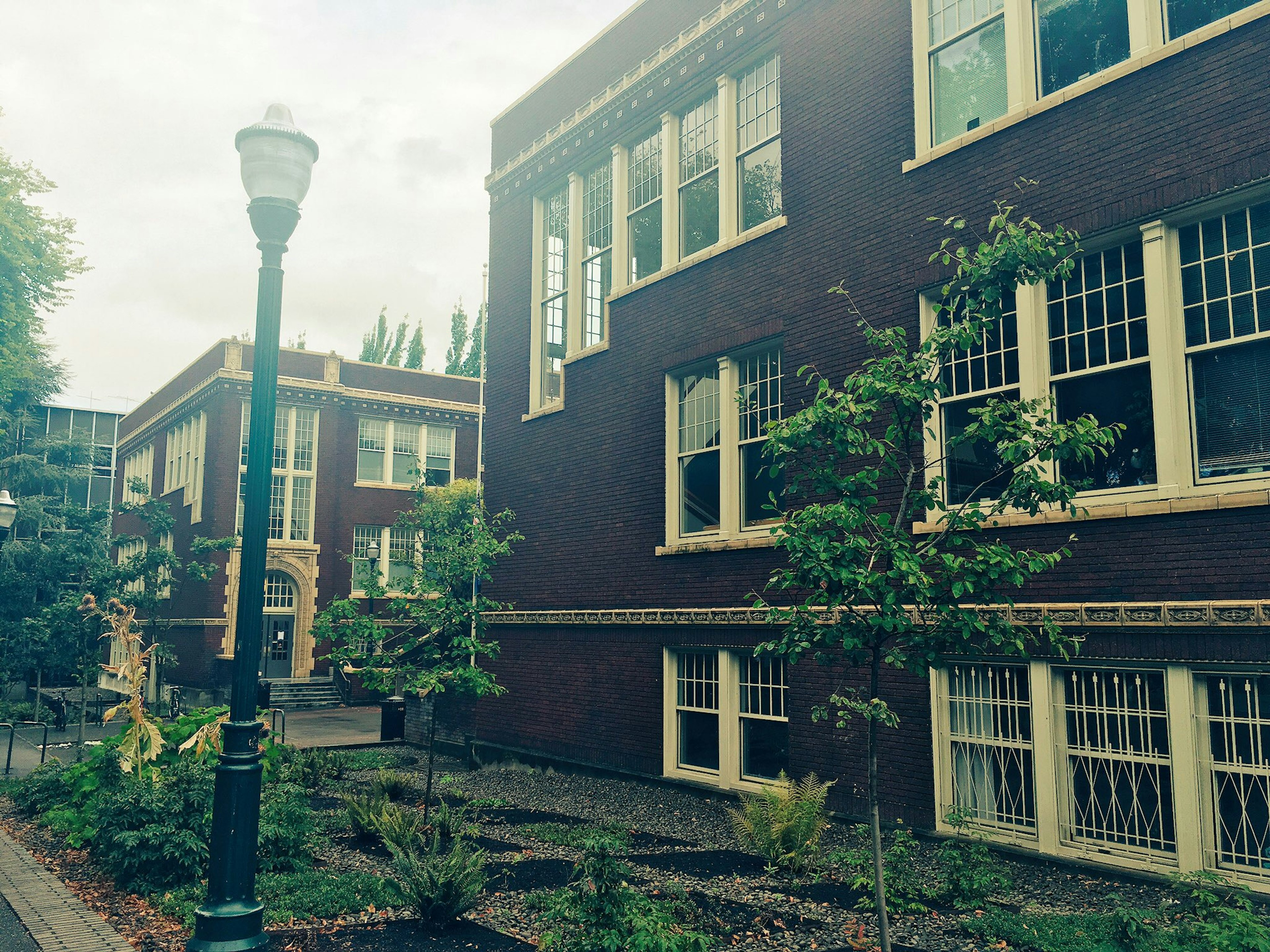 Historic brick school building with green trees and a lamppost