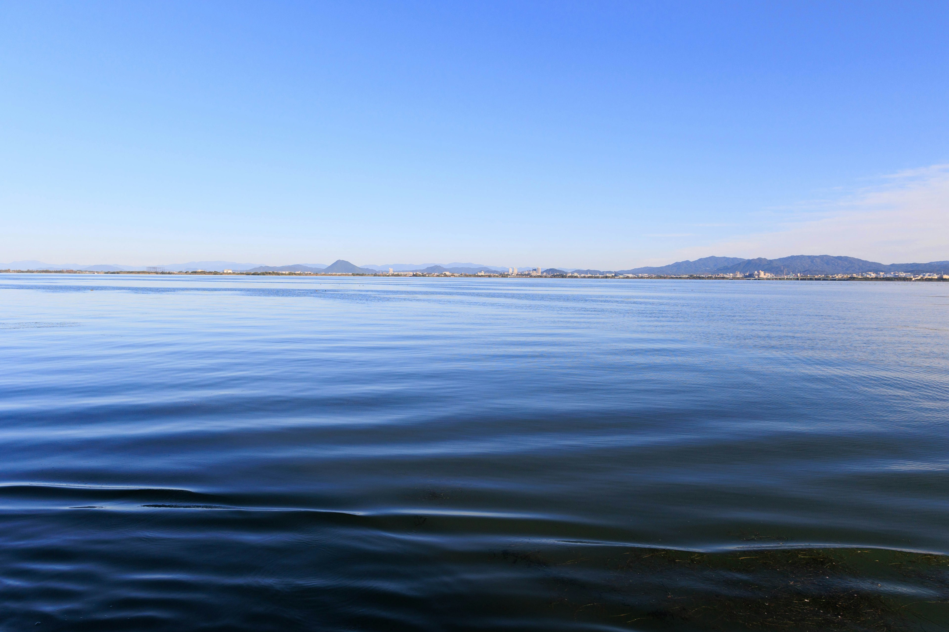 穏やかな海と青い空の風景 波紋が広がる水面 遠くに山々が見える