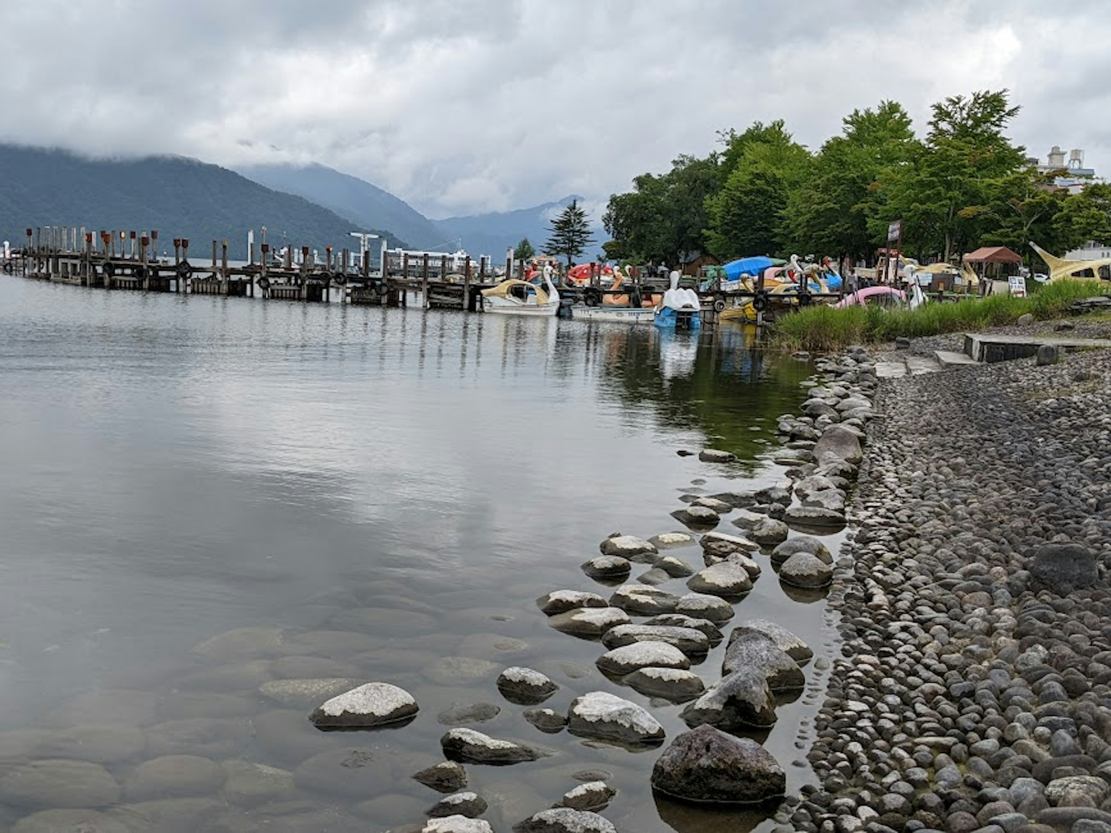 穏やかな湖の風景 船が停泊する桟橋 周囲には緑の木々と小石の岸