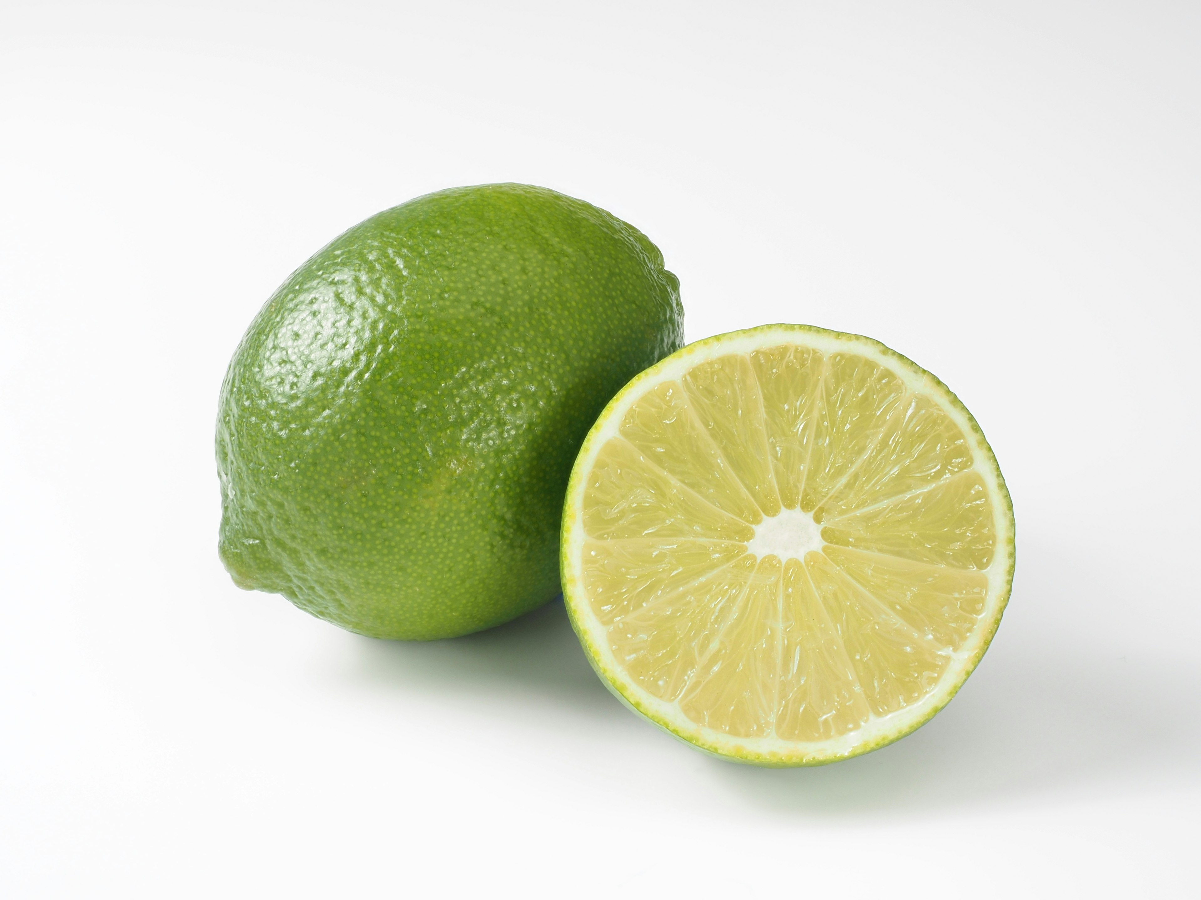 A whole lime next to a sliced lime showing its juicy interior