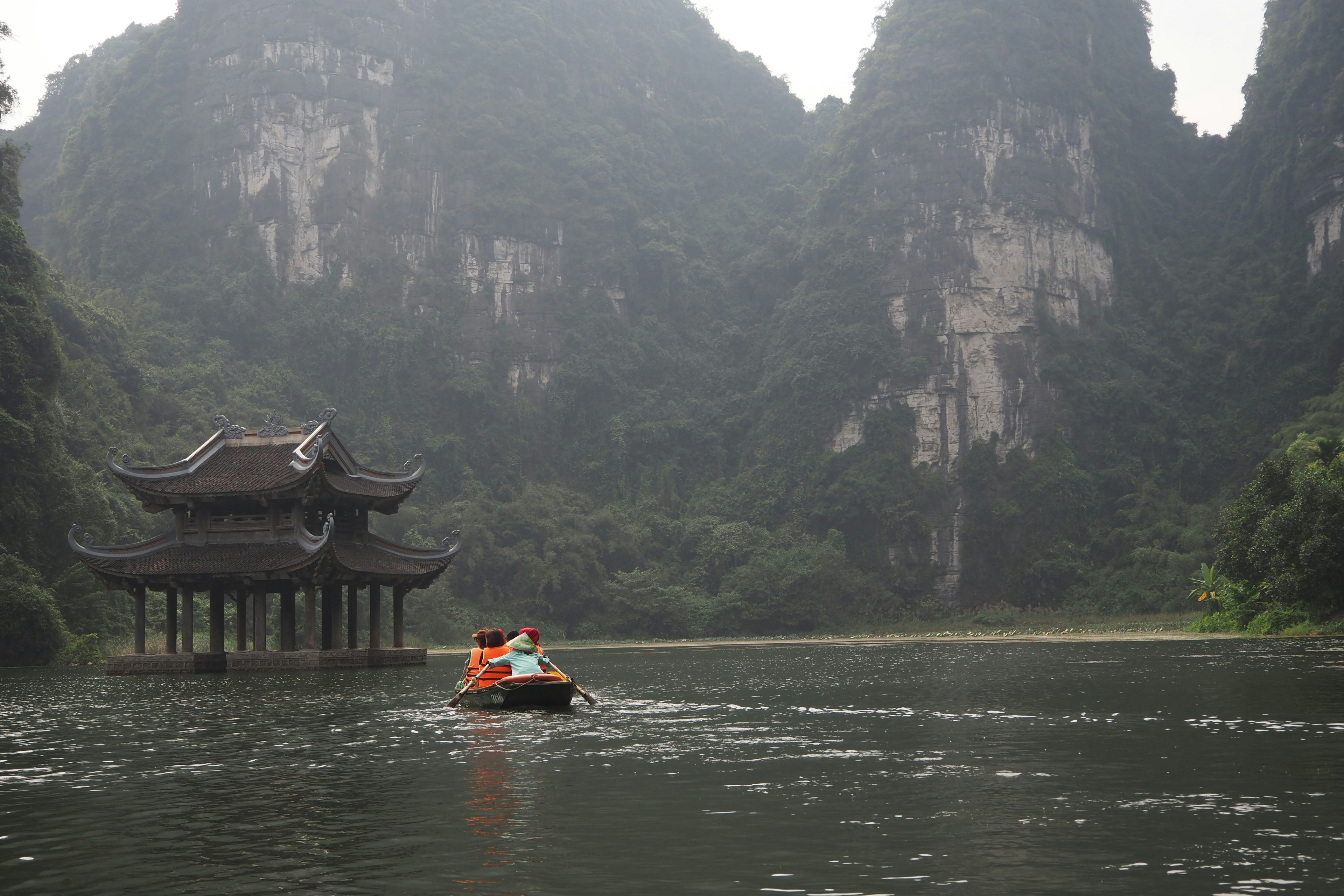 A boat navigating through misty mountains with an ancient structure by the river