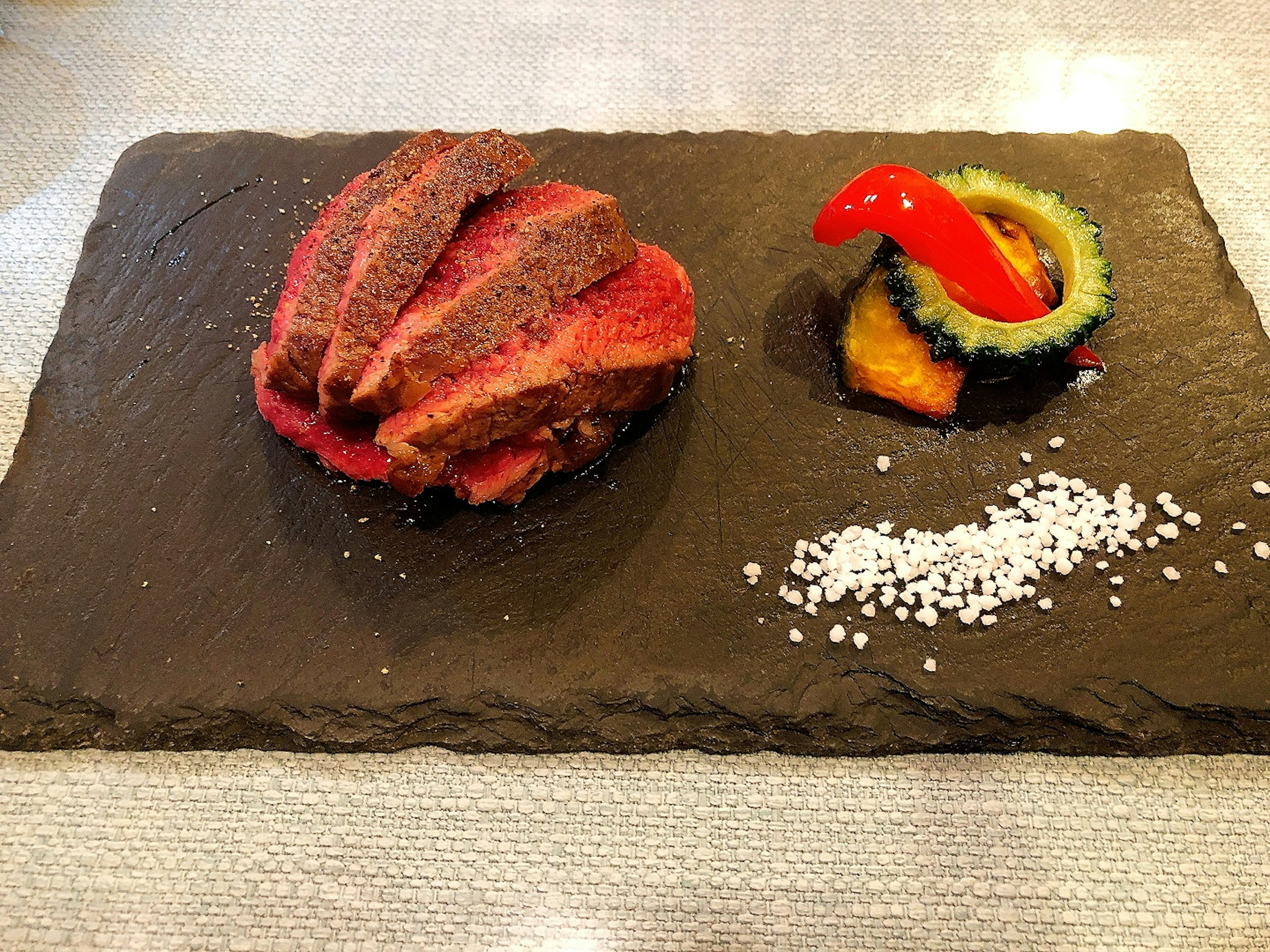 Beautifully plated meat dish on a black stone plate with colorful garnish