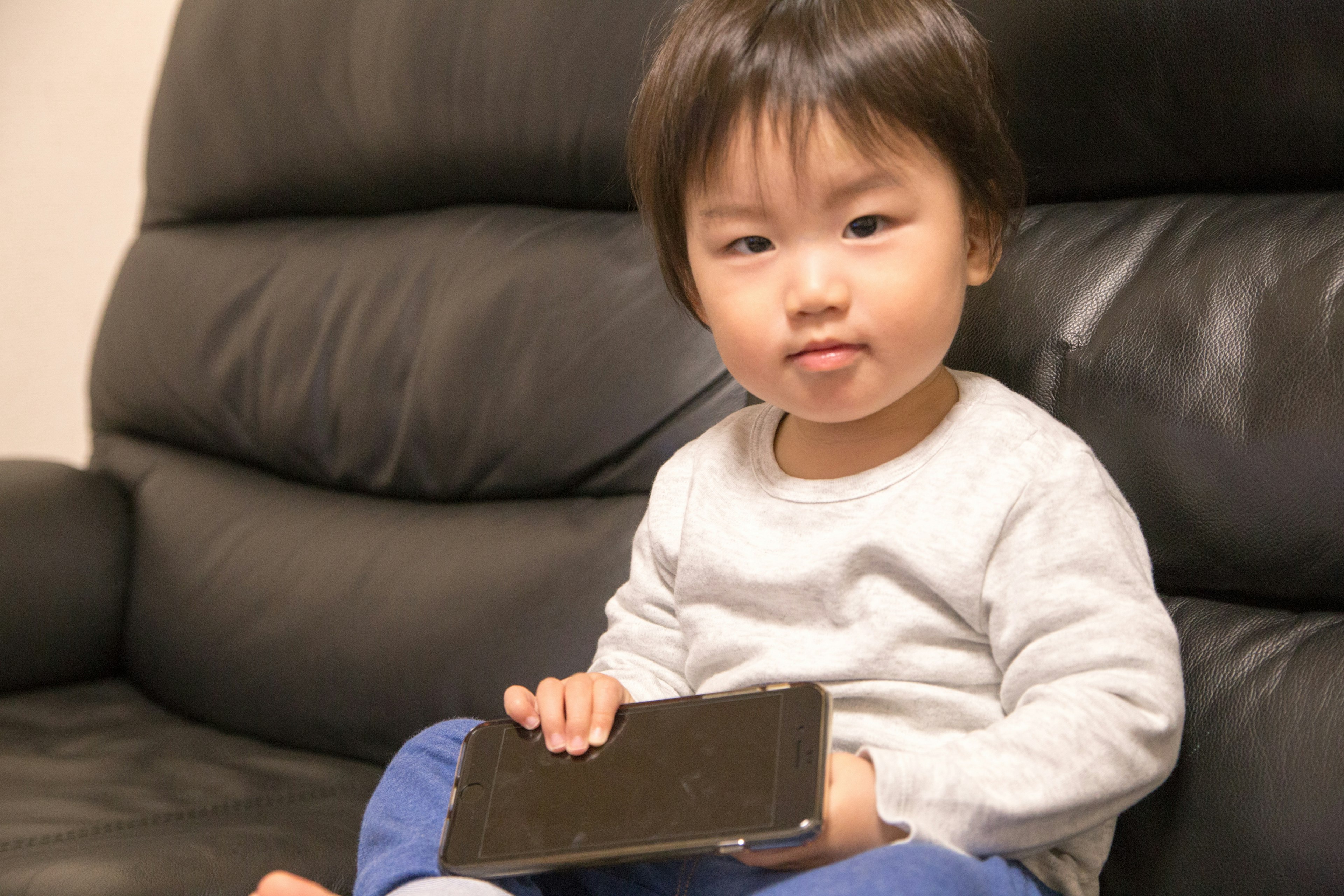 검은 소파에 앉아 스마트폰을 들고 있는 작은 아이