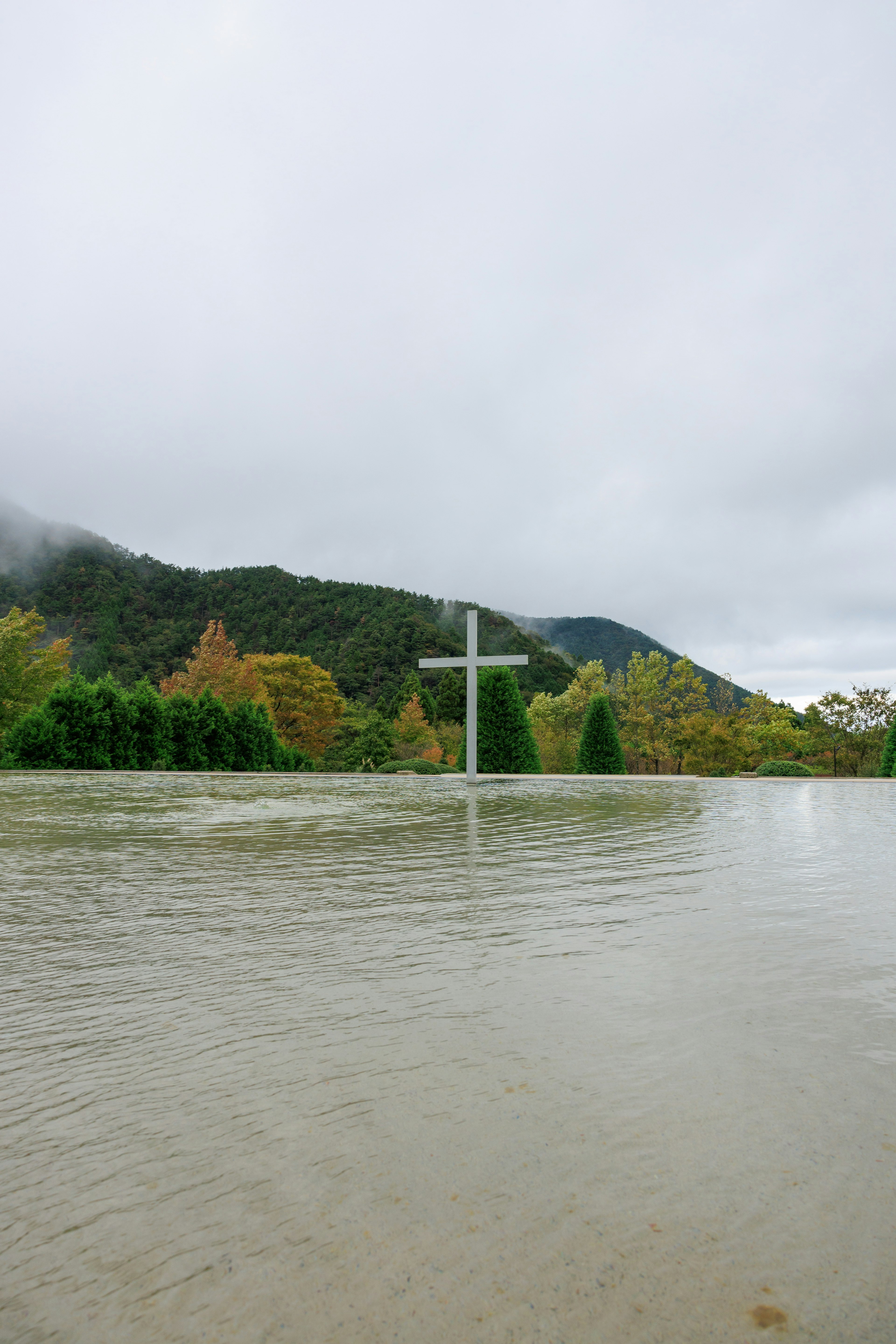 A submerged cross in water with green trees in the background