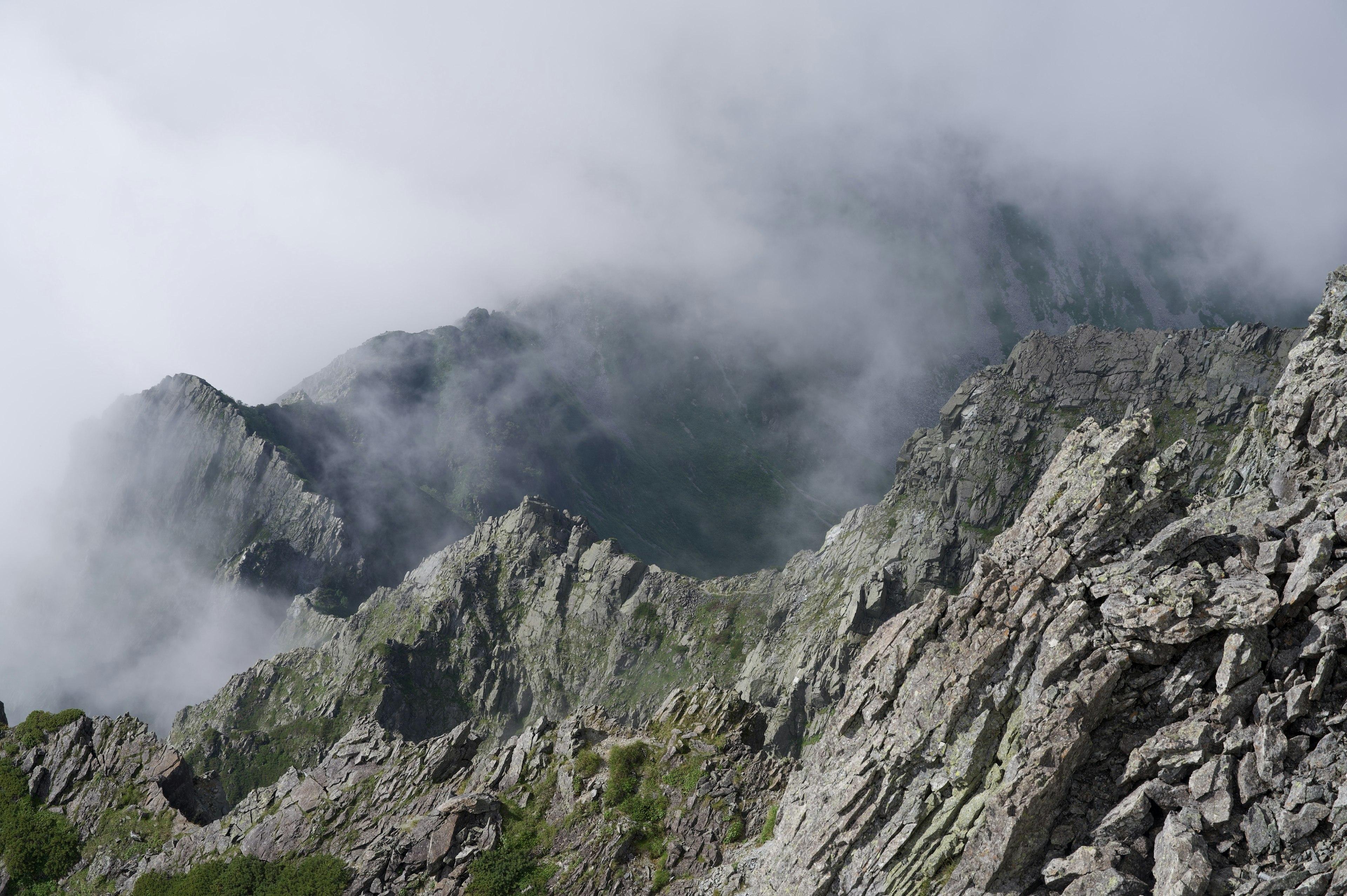 霧に包まれた山々の風景 鋭い岩の峰と緑の草地が見える