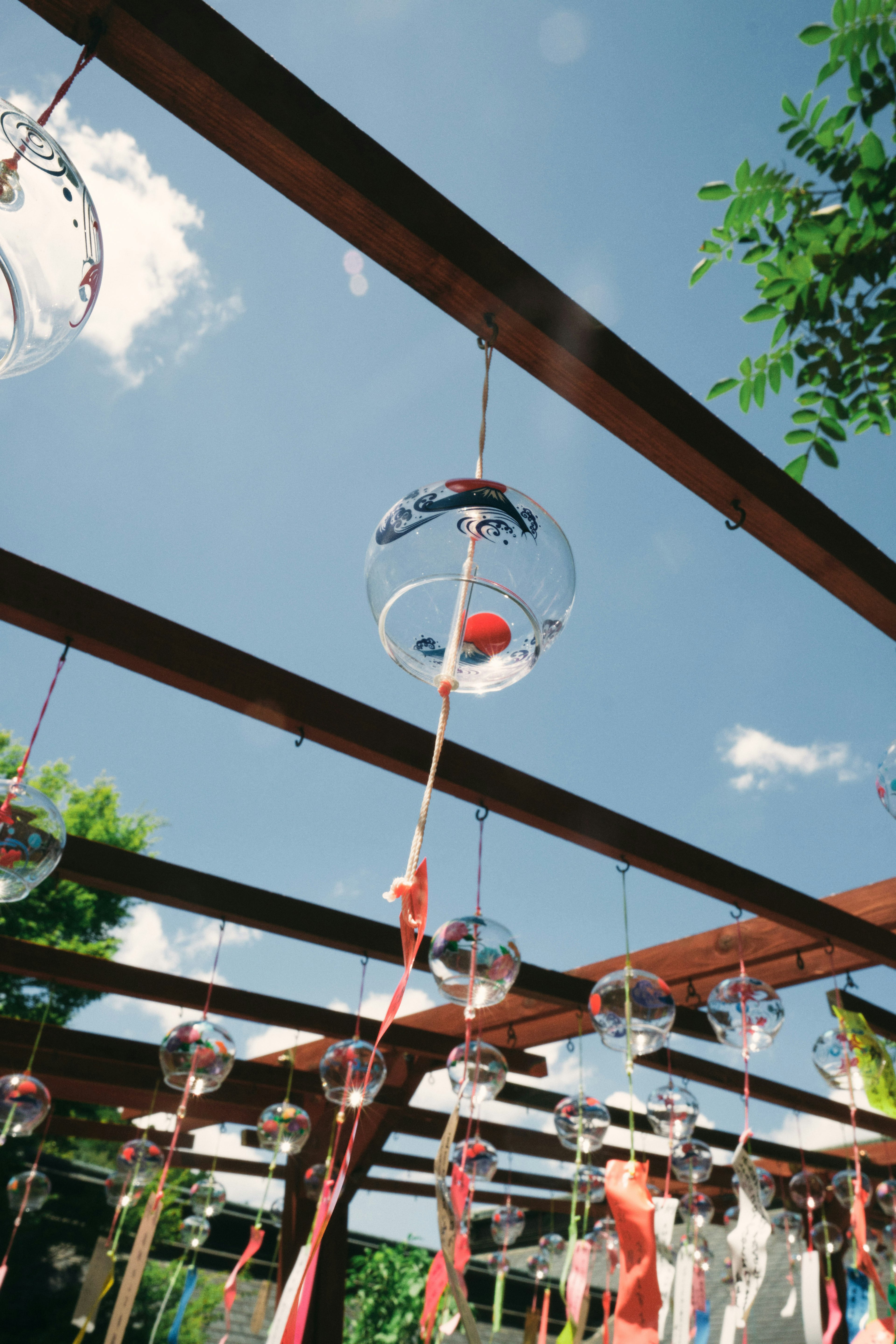 Objetos de vidrio transparente colgando bajo un cielo azul con cintas coloridas