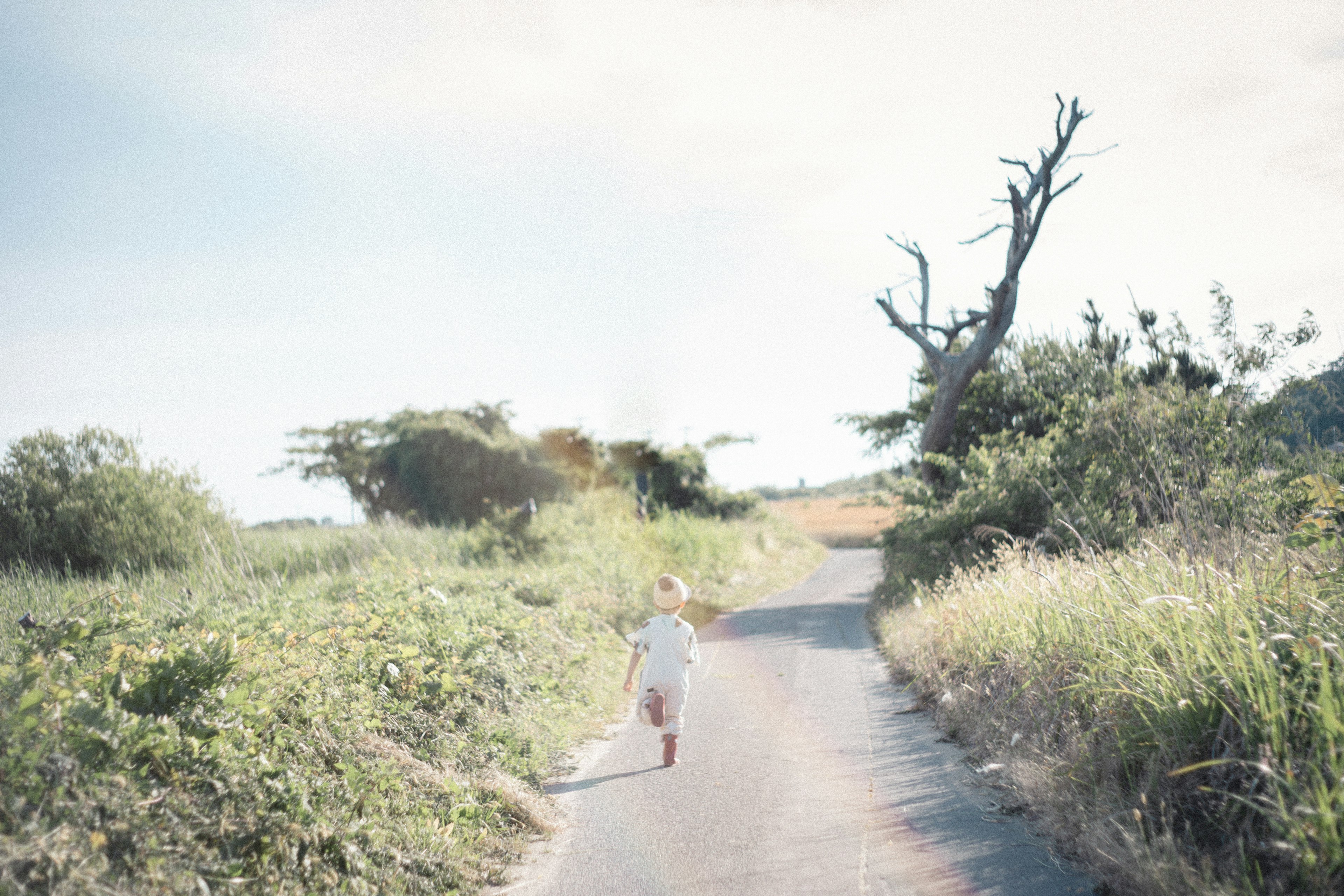 Child running on a rural road under a blue sky