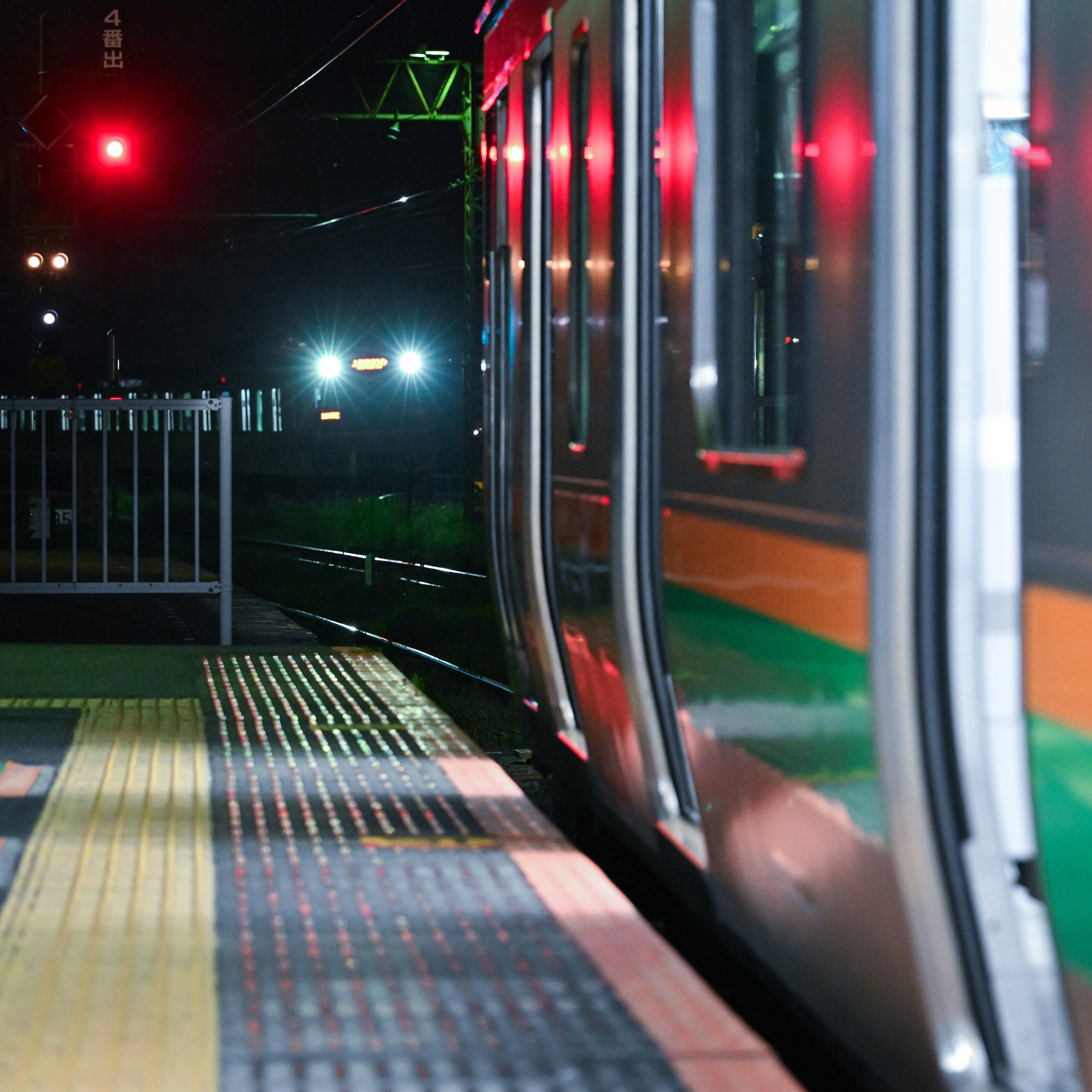 夜の駅で停車中の電車の側面と赤い信号の光